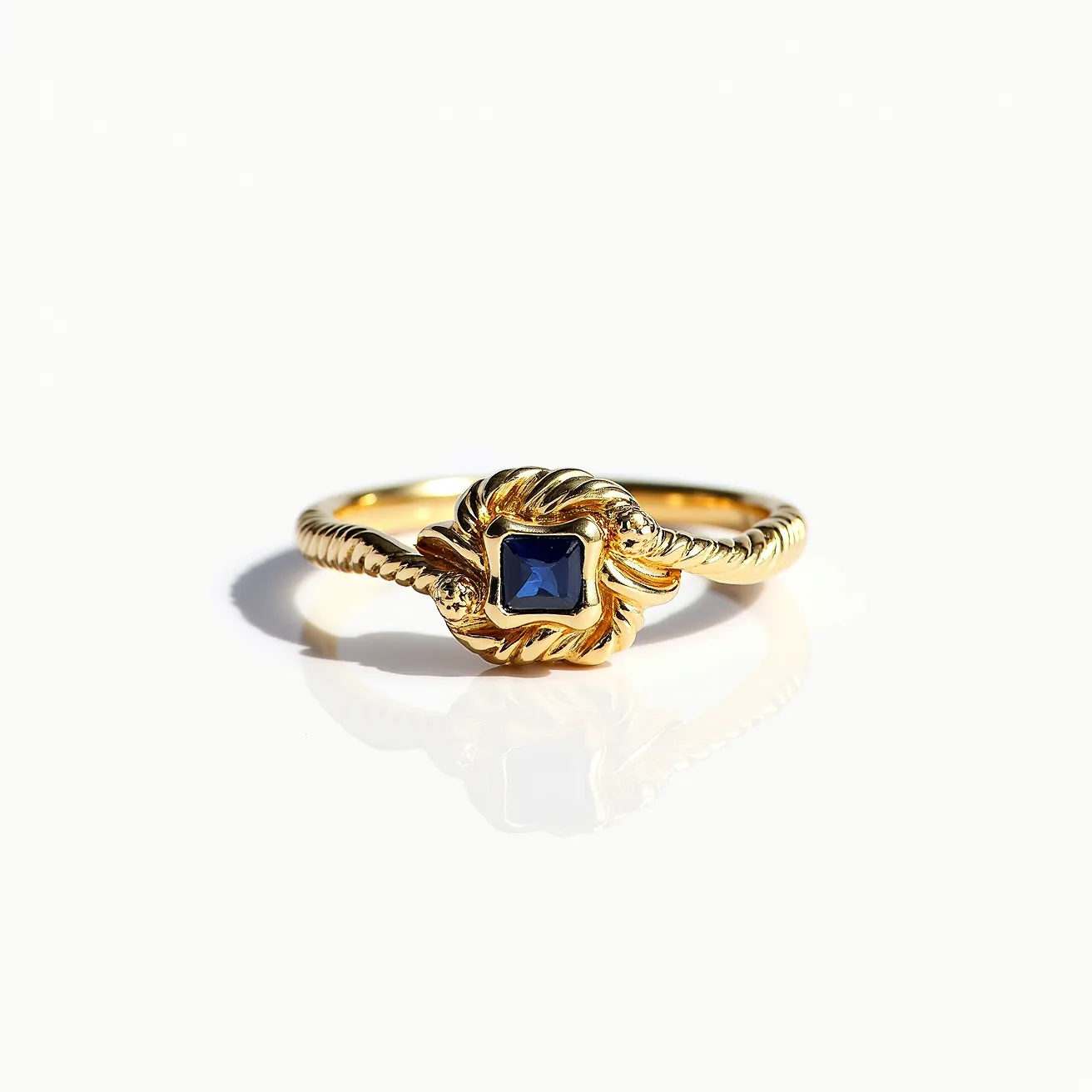 This knot ring features a beautifully twisted band crafted from gold. At its center, a striking blue square-cut gemstone, likely a sapphire, is set, enhancing the elegance with its deep color. The gem is securely held in a prong setting, seamlessly integrated into the intricate knot design. The twisted gold band and knot motif add an element of sophistication and charm to the piece, making it both a statement ring and a symbol of unity and eternity.