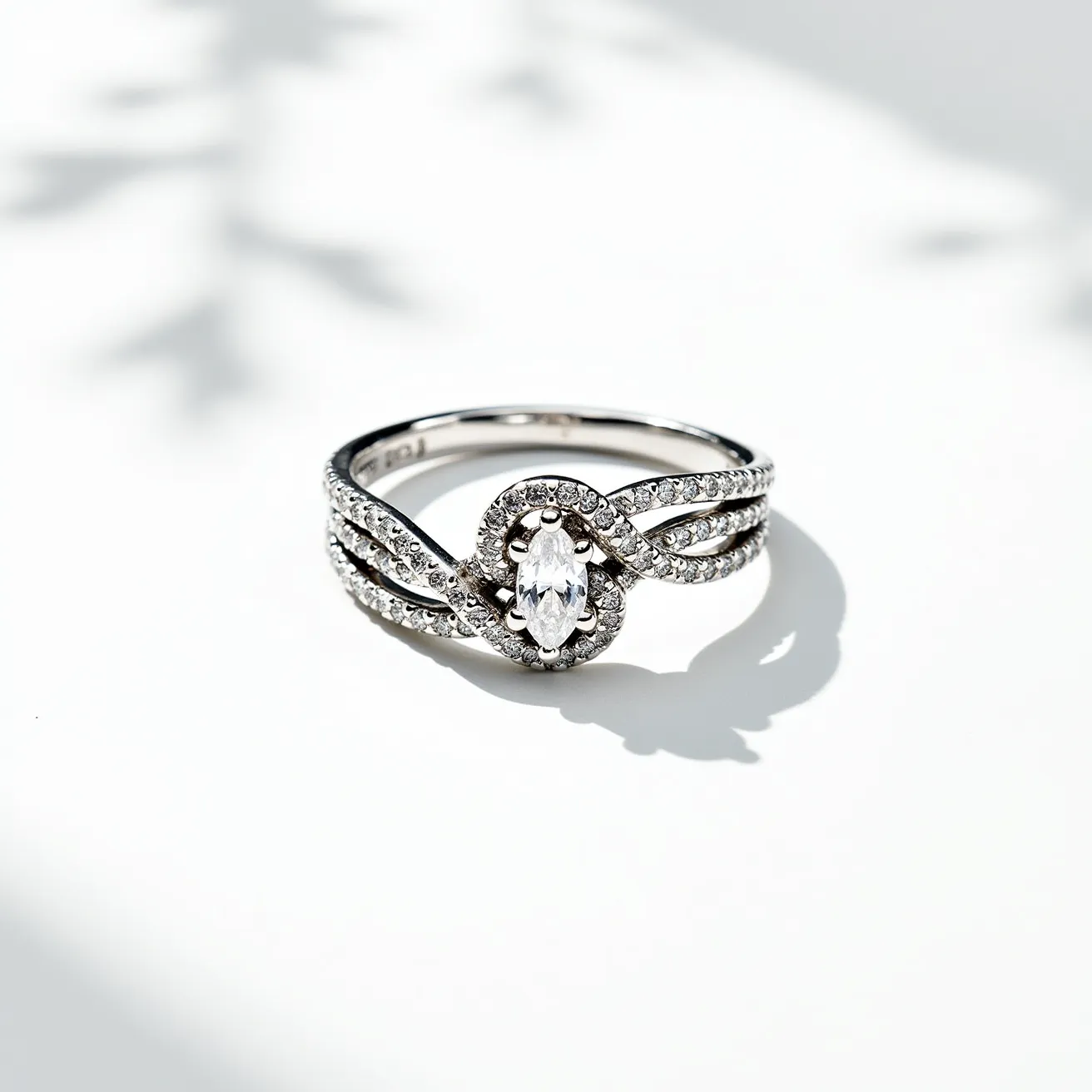 This knot ring features a sophisticated design crafted from a polished metal, likely white gold or platinum, accentuating its elegance. At its center, a marquise-cut gemstone is prominently displayed, meticulously set within a halo of smaller, round-cut stones that add a radiant sparkle. The band itself intertwines gracefully in a knot motif, with each strand adorned with additional smaller stones, enhancing the ring's intricate and luxurious appearance. The setting is secure, ensuring the central stone remains the focal point while seamlessly integrating with the band’s flowing design.