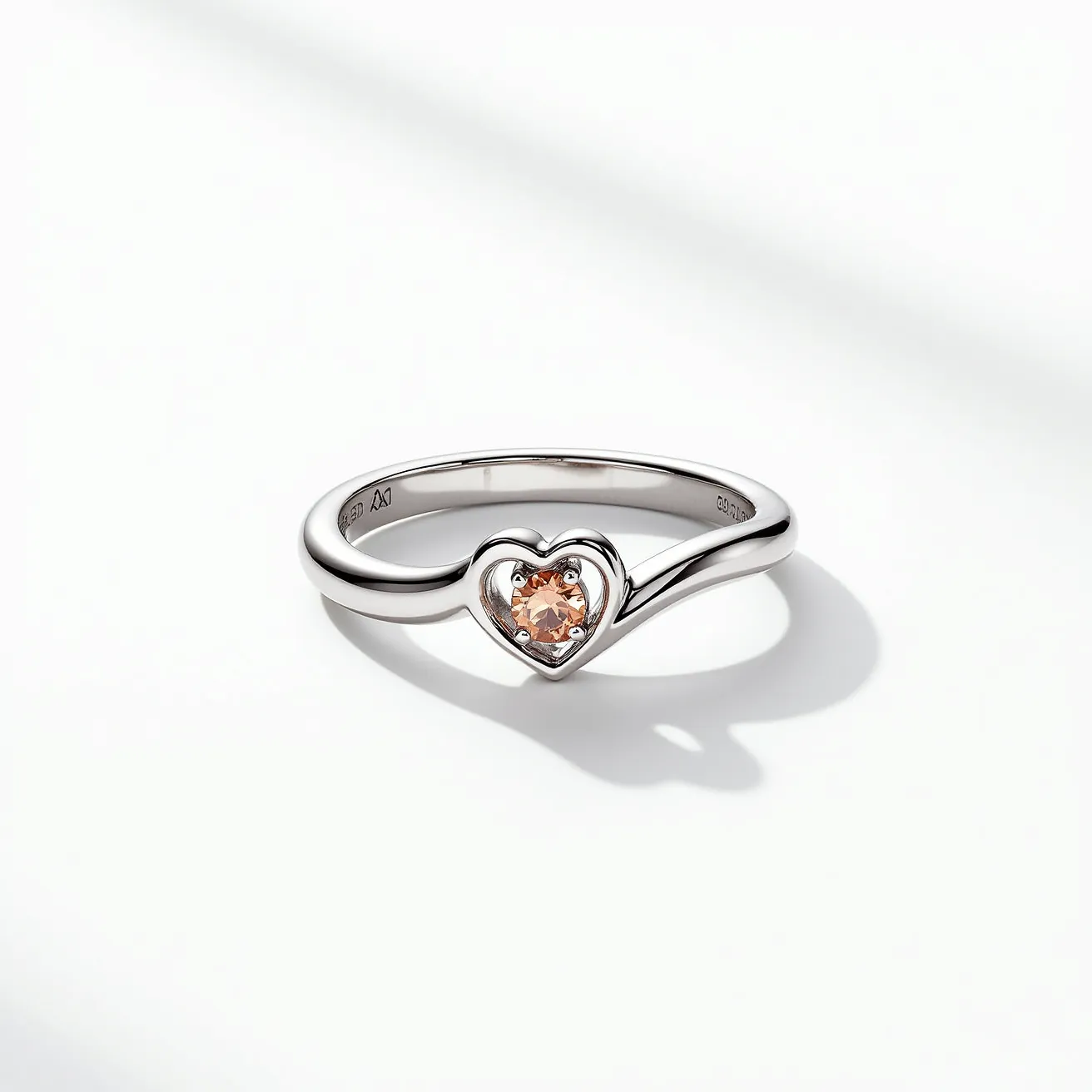 This love ring features a sleek, polished metal band crafted from a reflective material, possibly silver or white gold. The centerpiece is a heart-shaped setting that securely holds a single gemstone, which appears to be a tender peach or champagne color, suggesting it may be a morganite or similar stone. The gem is expertly cut in a brilliant style, enhancing its sparkle, and is secured within the heart setting by multiple prongs for stability and elegance. The smooth band is unbroken and simple, drawing focus to the romantic heart detail that characterizes the ring's design.