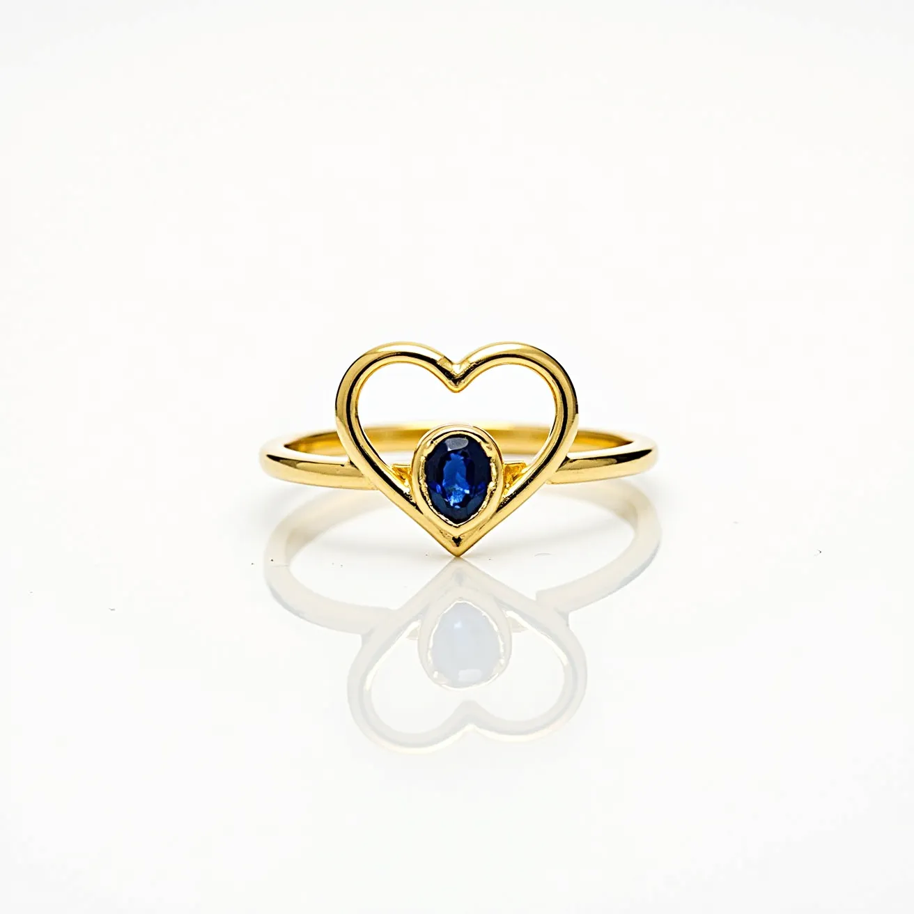 This love ring is crafted from polished gold and features an elegant open-heart design at its center. Within the heart, an oval-cut blue gemstone is securely set, adding a vibrant splash of color that contrasts beautifully with the golden setting. The gem is held in place with a bezel setting, ensuring both security and a sleek appearance. The ring is a seamless piece without any visible clasp or attachment mechanism, emphasizing its simple yet sophisticated design.