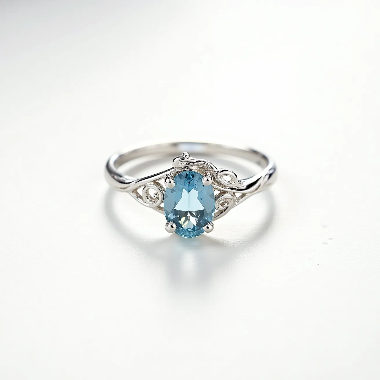 This March birthstone ring features a prominent oval-cut aquamarine gemstone, which exudes a soft blue hue synonymous with the month. The stone is elegantly set in a prong setting, enhancing its reflective qualities and securing it firmly in place. The band, likely crafted from silver or white gold, showcases intricate scrollwork details that flow gracefully on either side of the aquamarine, adding to the ring's overall sophistication. The combination of the gemstone's clarity and the delicate metalwork creates a timeless piece that does not incorporate any additional clasps or attachments.