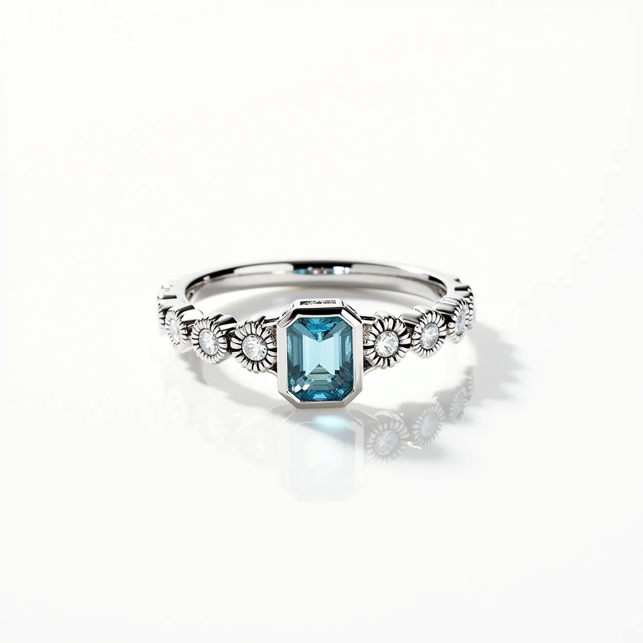 This March birthstone ring features an elegant aquamarine gemstone, cut in a refined emerald shape, set prominently at the center. The stone is encased in a delicate bezel setting that highlights its cool blue hue. The band is crafted from a polished silver-toned metal, adorned with intricate floral motifs accented by small, round diamonds set in each flower's center, adding sparkle and detail to the overall design. The craftsmanship of the ring emphasizes artisanal design with a harmonious blend of simple elegance and subtle luxury.