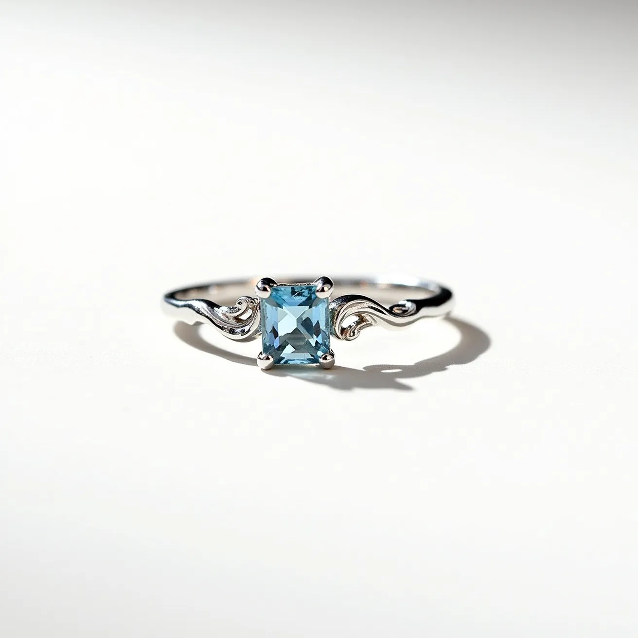 This March birthstone ring features an elegantly designed setting crafted from polished silver, showcasing a striking aquamarine gemstone at its center. The stone is cut in a rectangular or emerald shape, enhancing its natural clarity and reflective properties. It is securely held in place by four prongs, ensuring both durability and a classic aesthetic. The band itself is adorned with gracefully swirling embellishments that add a touch of sophistication to the overall design, perfectly complementing the bright blue hue of the aquamarine.