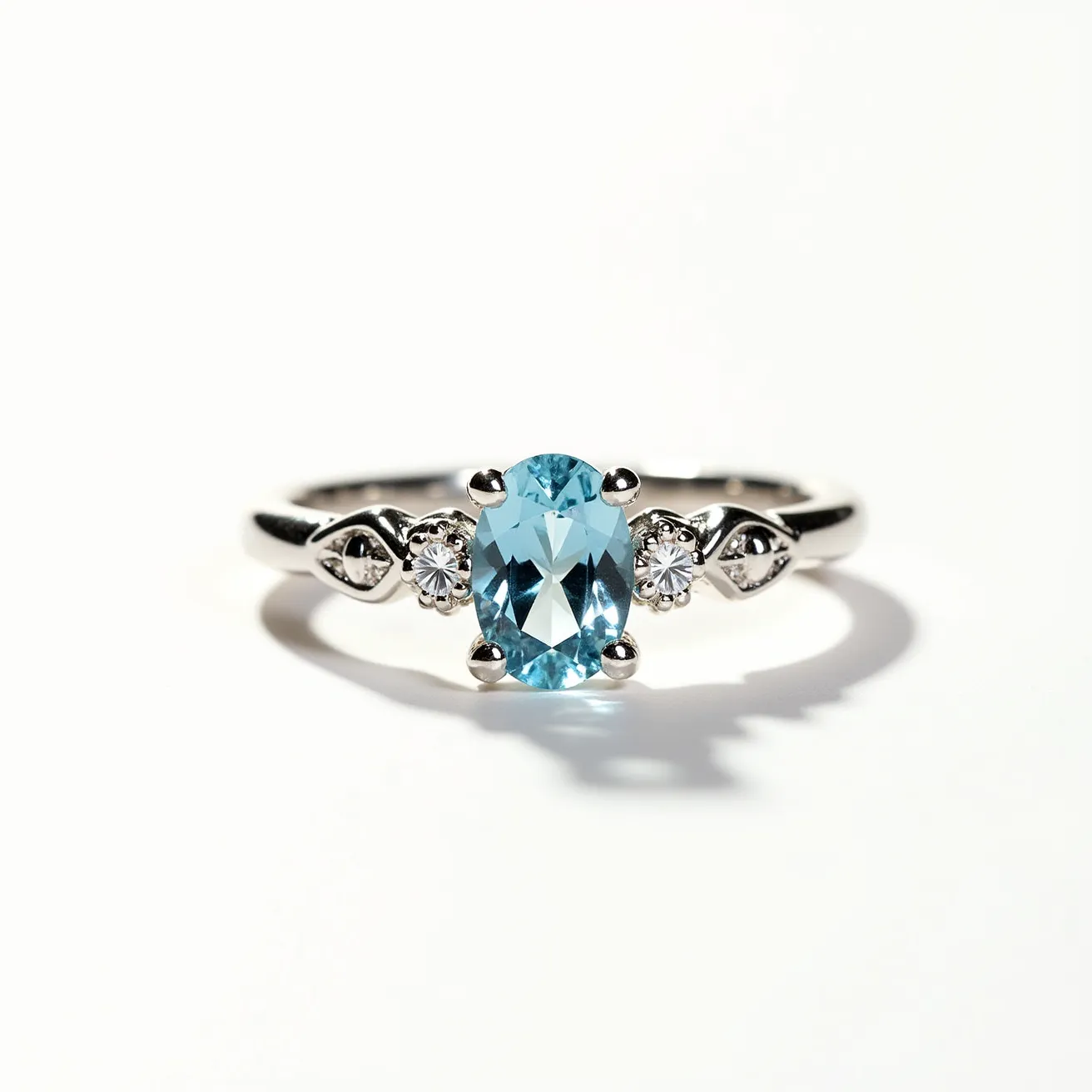 This March birthstone ring showcases a beautiful aquamarine gemstone as its centerpiece, which is an oval cut, characterized by its light blue hue. The aquamarine is securely held in a four-prong setting, allowing the stone to catch and reflect light beautifully. Flanking the central stone are two smaller, round-cut diamonds, each set in a traditional prong setting, adding a touch of sparkle and elegance to the design. The band is crafted from a polished white metal, likely white gold or platinum, which enhances the overall sophistication and complements the cool tones of the aquamarine and diamonds.