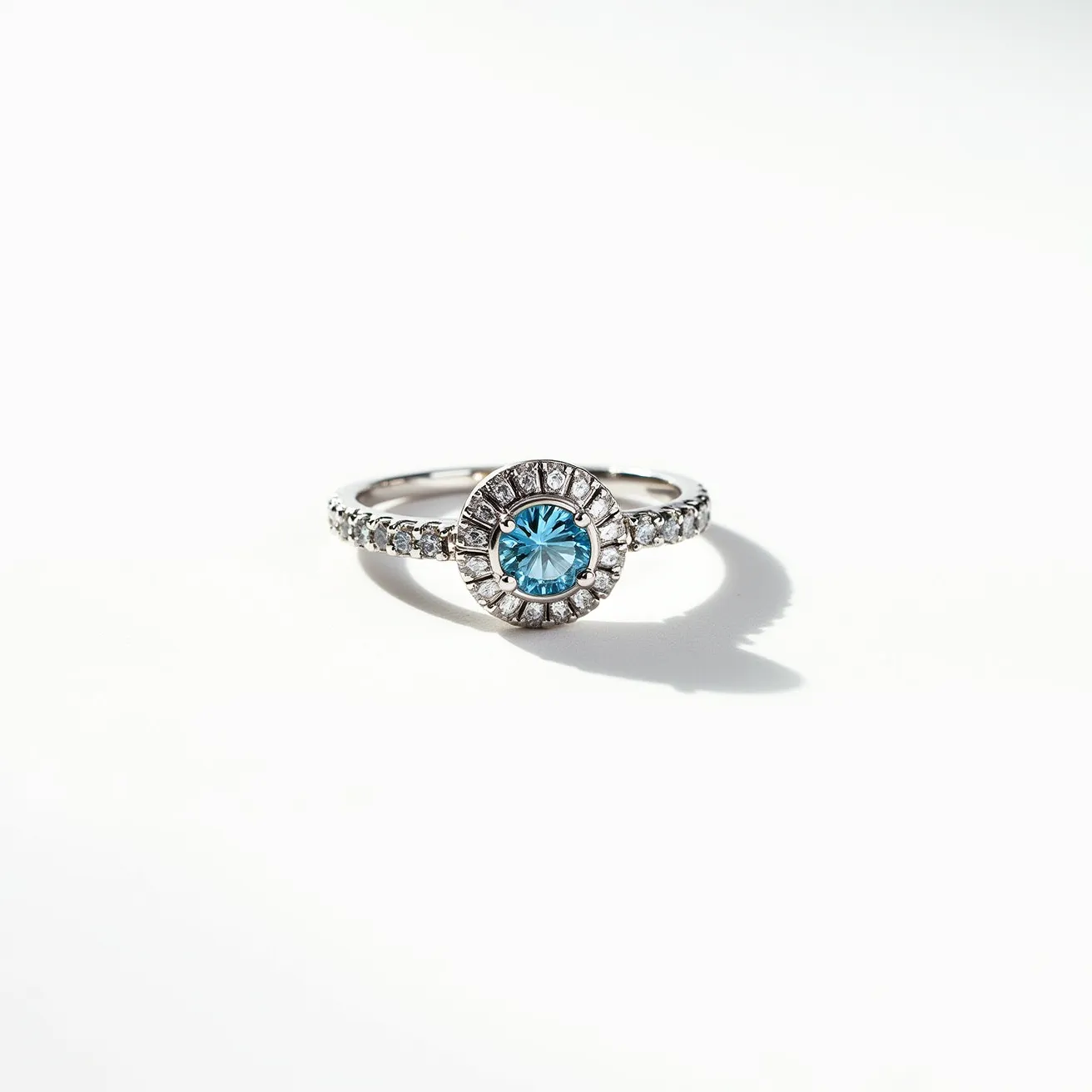 This March birthstone ring showcases an elegant aquamarine gemstone, cut in a round fashion and set at the center of the ring. Surrounding the aquamarine is a halo of smaller, brilliant-cut diamonds, adding a touch of sparkle and enhancing the centerpiece. The band itself is crafted from silver or white gold, which complements the cool tones of the aquamarine and diamonds, and is further adorned with a series of small diamonds that are set in a pave style, providing a continuous shimmer around the finger. The overall design of the ring is delicate and refined, making it a sophisticated piece that highlights the beauty of the March birthstone.