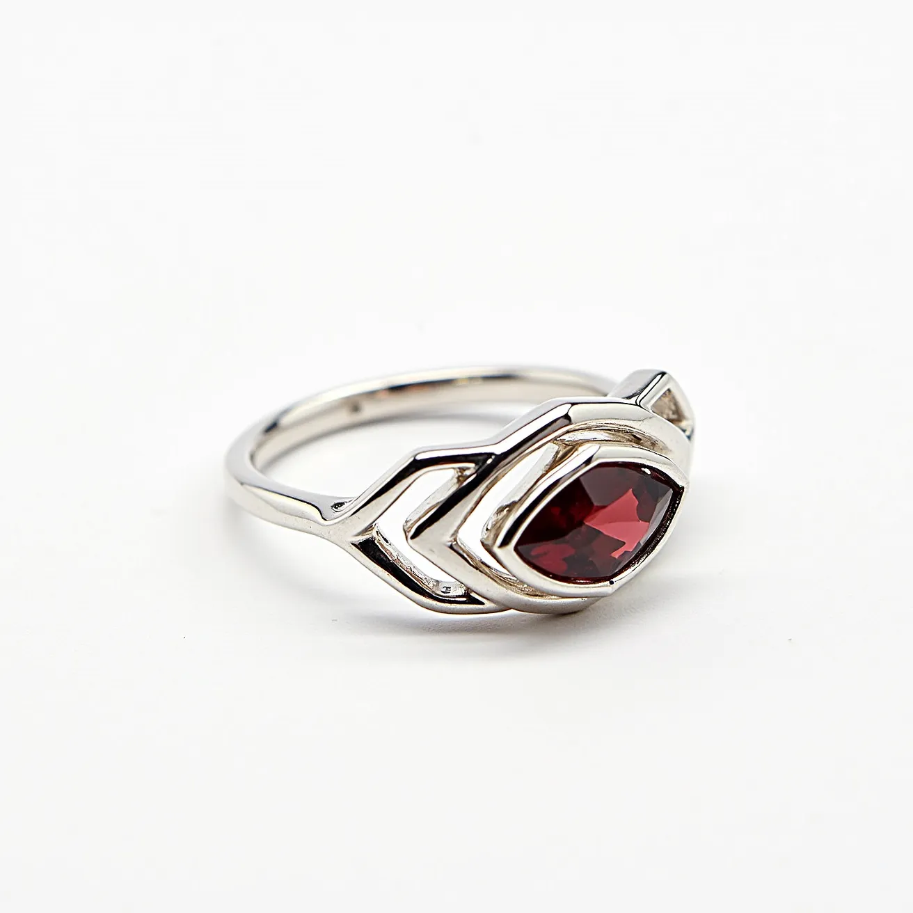 This March birthstone ring features a distinctive design with a marquise-cut deep red stone, elegantly set in a polished metal band. The stone is embraced by a stylized double-chevron setting, which enhances its prominence and adds a modern touch to the classic silhouette. The band is smooth and gleaming, likely crafted from a durable metal, providing both strength and aesthetic appeal. The stone appears to be securely held in the setting, ensuring that the ring is both attractive and practical for everyday wear.