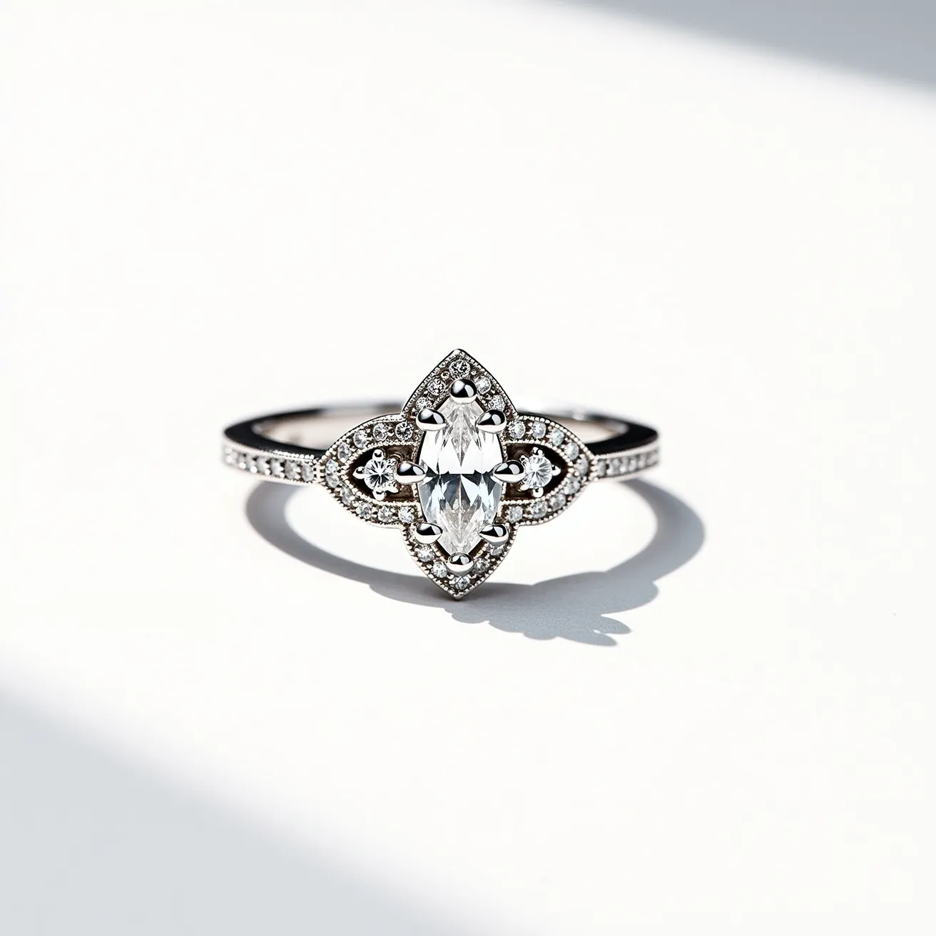 This marquise diamond ring features a central marquise-cut diamond set within an intricately designed setting that includes additional small diamonds around the centerpiece. The band is crafted from a white metal, likely white gold or platinum, adorned with a line of small, sparkling diamonds. The setting securely holds the central diamond in place with visible prongs that elegantly blend into the overall floral-inspired design. The ring combines sophistication with contemporary elegance, making a striking impact through its detailed craftsmanship and the choice of shimmering materials.