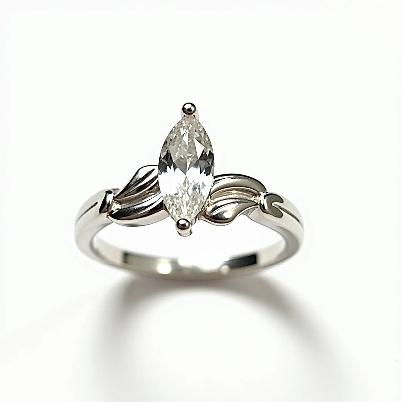 This marquise diamond ring features a prominent marquise-cut diamond set horizontally in a sleek, elegant design. The diamond is secured by a prong setting, allowing maximum light to enhance its brilliance. The band appears to be made of polished metal, likely platinum or white gold, enhancing the overall shine and luxury of the piece. The setting includes intricate metalwork on the sides, adding a decorative touch to the band and complementing the diamond centerpiece. The combination of the marquise cut and the detailed craftsmanship creates a sophisticated and timeless appearance.