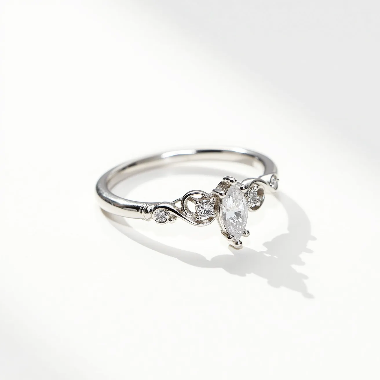 This marquise diamond ring features a central marquise-cut diamond set in an elegant prong setting, accentuating its distinctive, elongated shape. The band appears to be crafted from a polished metal, likely platinum or white gold, adding a sleek, reflective quality. The setting includes additional small round diamonds on either side, enhancing the ring's overall sparkle and sophisticated design. Curved metalwork on the band adds a touch of intricate detail, seamlessly integrating the side stones in a graceful flow. The open gallery design allows light to pass through, maximizing the brilliance of the stones.