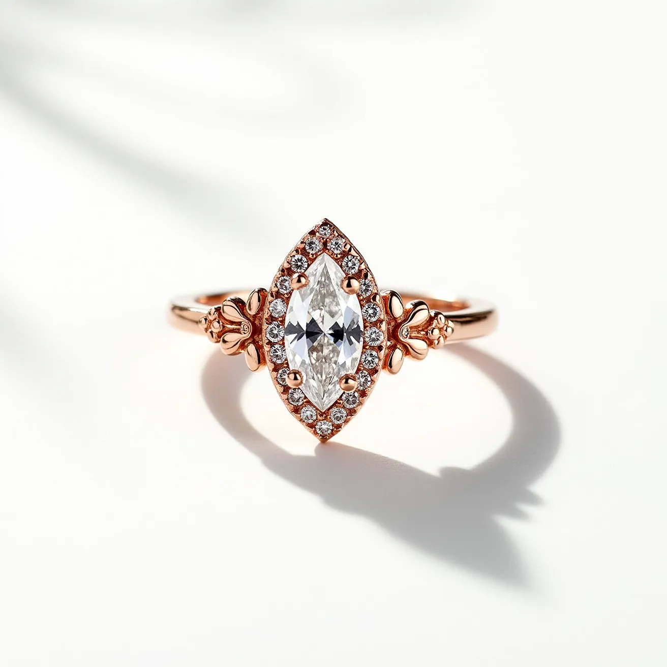 This marquise diamond ring showcases a stunning marquise-cut diamond as the centerpiece, surrounded by a halo of smaller round diamonds that enhance its sparkle and elegance. The ring features a rose gold band, which adds a warm, luxurious tone and complements the brilliance of the diamonds. The band is adorned with intricate, floral-inspired detailing on either side of the centerpiece, adding an element of sophistication and unique charm. The marquise diamond is secured in place with four prongs, ensuring stability and emphasizing the stone's elongated shape. This exquisite combination of materials and craftsmanship makes the ring a striking piece of jewelry.