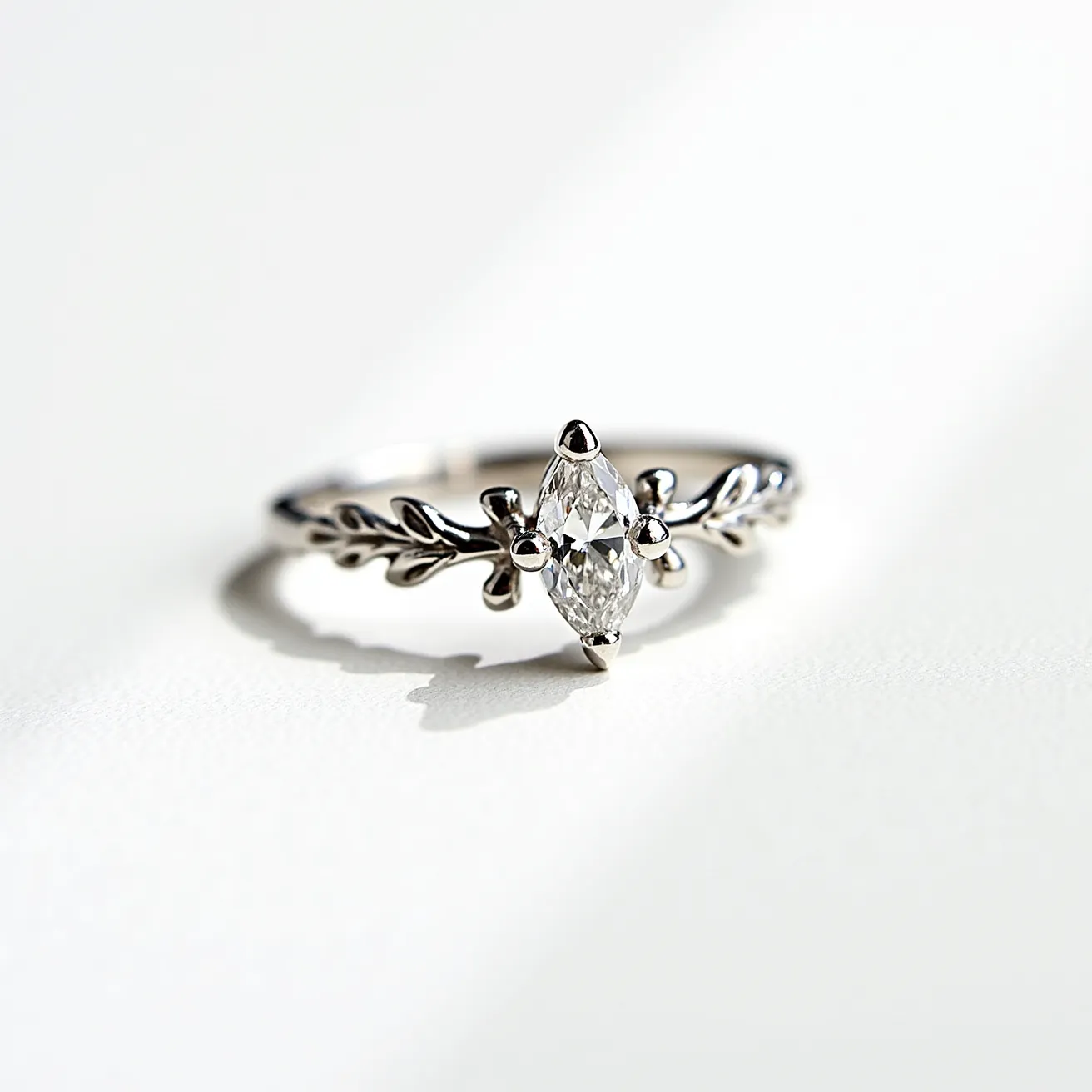 This marquise engagement ring features a beautifully cut marquise diamond set at its center. The stone is securely held in place by a four-prong setting, which allows for maximum light exposure and brilliance. The band, made of polished white gold or platinum, adds a sense of elegance and sophistication to the ring. The band design includes a delicate leaf motif that wraps around the finger, complementing the central diamond with an organic and graceful aesthetic.