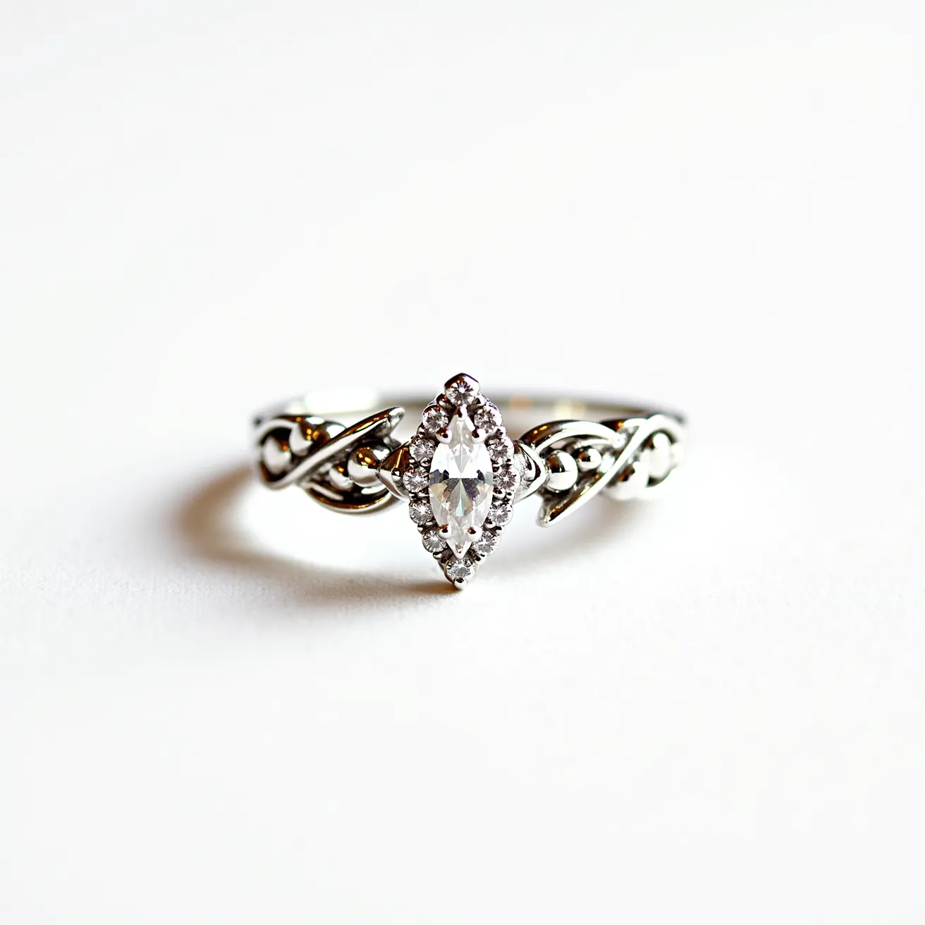 This marquise engagement ring features a central marquise-cut diamond, set into a delicate and intertwining band of white gold. The band displays an elegant, intricate design reminiscent of Celtic motifs, enhancing the overall aesthetic with its graceful curves and loops. The diamond is securely set in a prong setting, which allows it to capture maximum light, highlighting its brilliance. Surrounding the central stone, smaller accent diamonds create a halo effect, adding to the ring’s sparkle and sophistication. The materials and craftsmanship combine to form a timeless piece that exudes both elegance and charm.