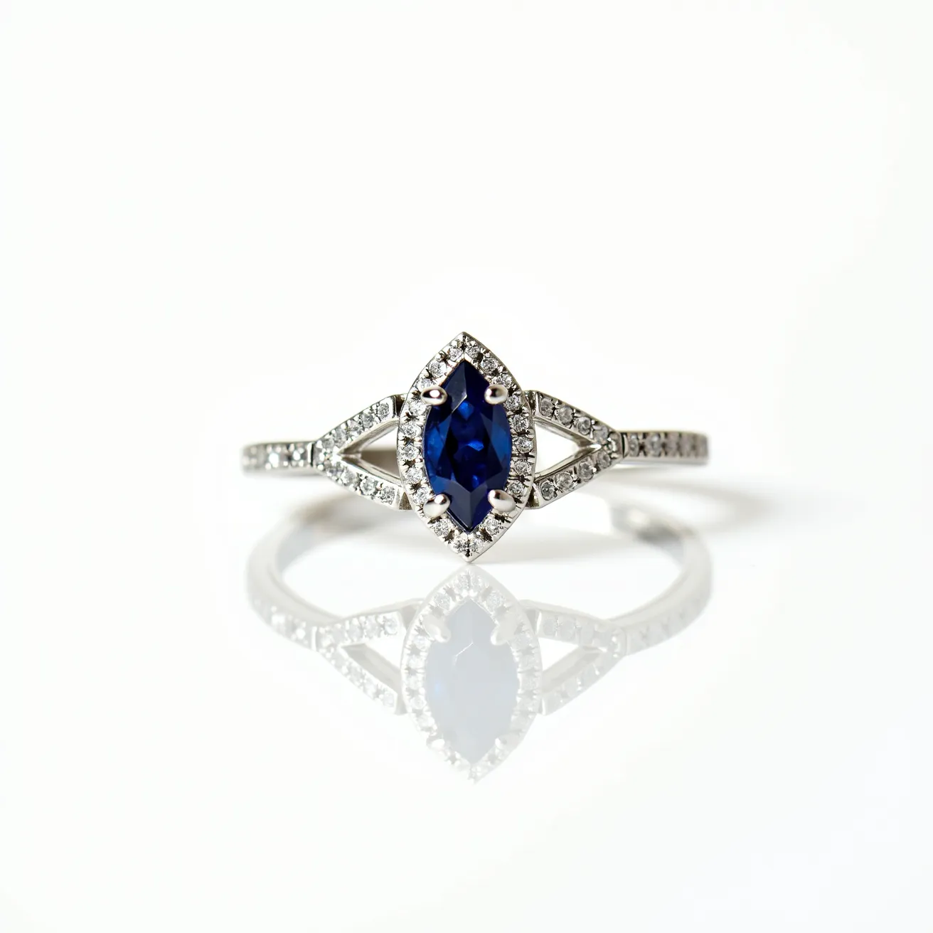 This marquise engagement ring features a striking blue marquise-cut gemstone set in the center, surrounded by a halo of small round diamonds that enhance its elegance. The band is crafted from a polished metal, likely white gold or platinum, and is adorned with additional small round diamonds that extend halfway down each side. The center stone is secured with claw prongs, ensuring it is held firmly in place while maximizing the visibility of the gemstone. The setting offers a modern yet timeless appeal, gracefully blending classic design elements with contemporary style.