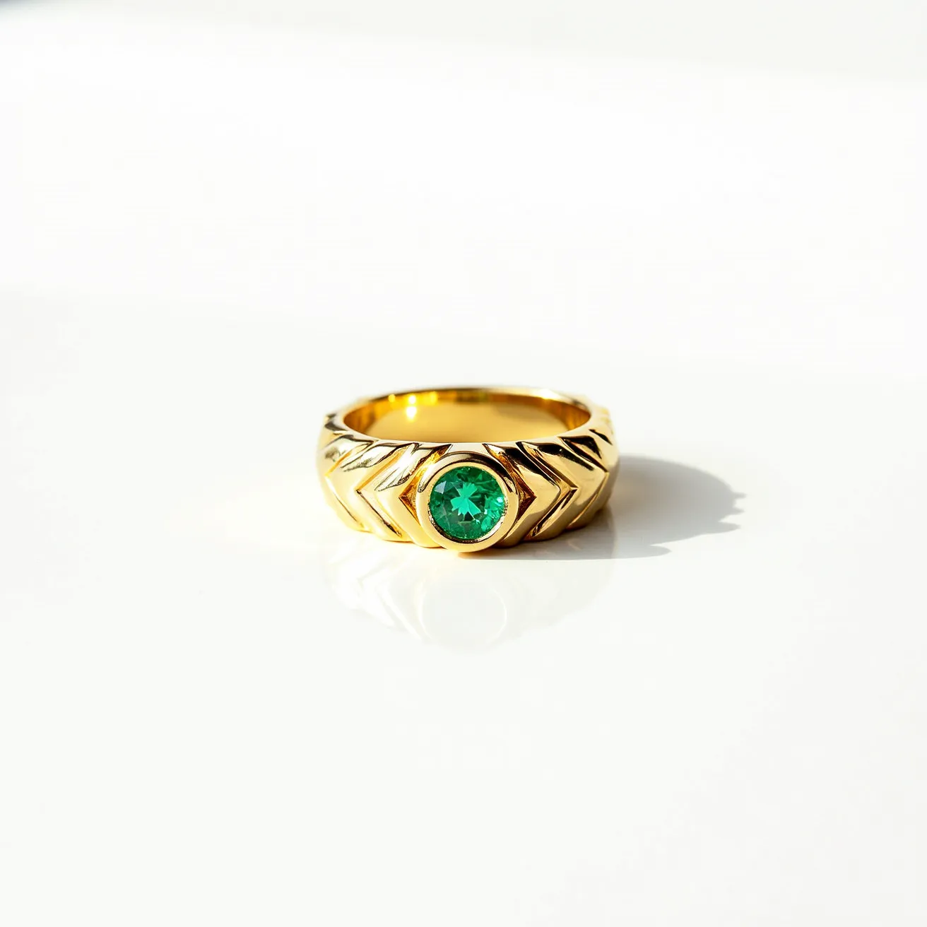 This men's engagement ring is crafted in yellow gold, featuring a prominent round-cut green gemstone, possibly an emerald, securely set in a bezel setting at its center. The band showcases an intricate chevron pattern, adding texture and design to the overall piece. The ring has a solid and continuous structure, reflective of attentive craftsmanship and style for a sophisticated look.