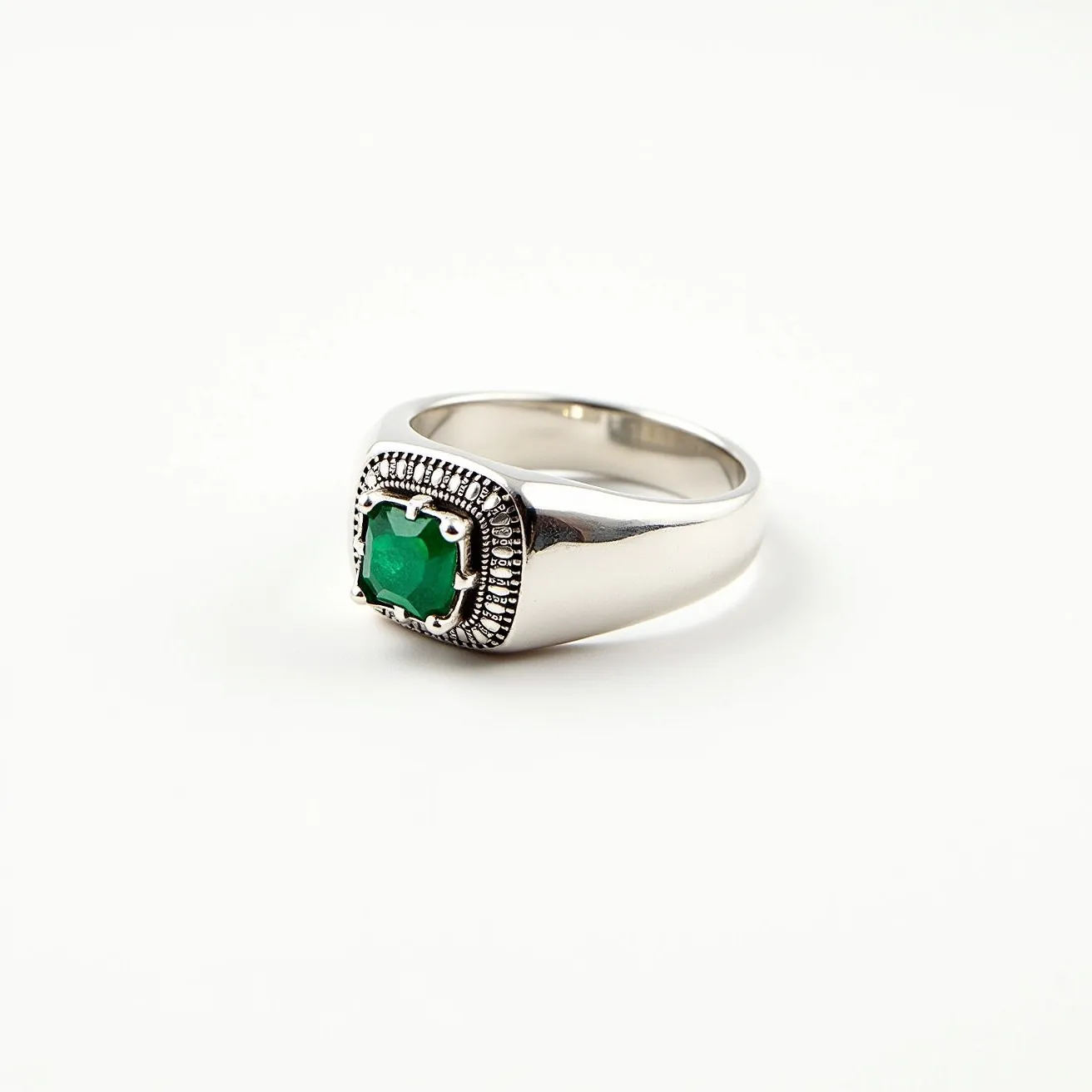 This men's pinky ring features a striking square-shaped green gemstone set at its center, likely an emerald, which is prominently displayed in a four-prong setting. The ring itself is crafted from a polished metal, possibly white gold or platinum, lending it a sleek and reflective appearance. Surrounding the gemstone is a decorative, textured design that adds complexity and elegance to the overall aesthetic. The band is sturdy and thick, imparting a sense of durability and masculinity. There is no visible clasp or attachment, as the ring is designed to be a singular piece meant for easy slip-on wear.