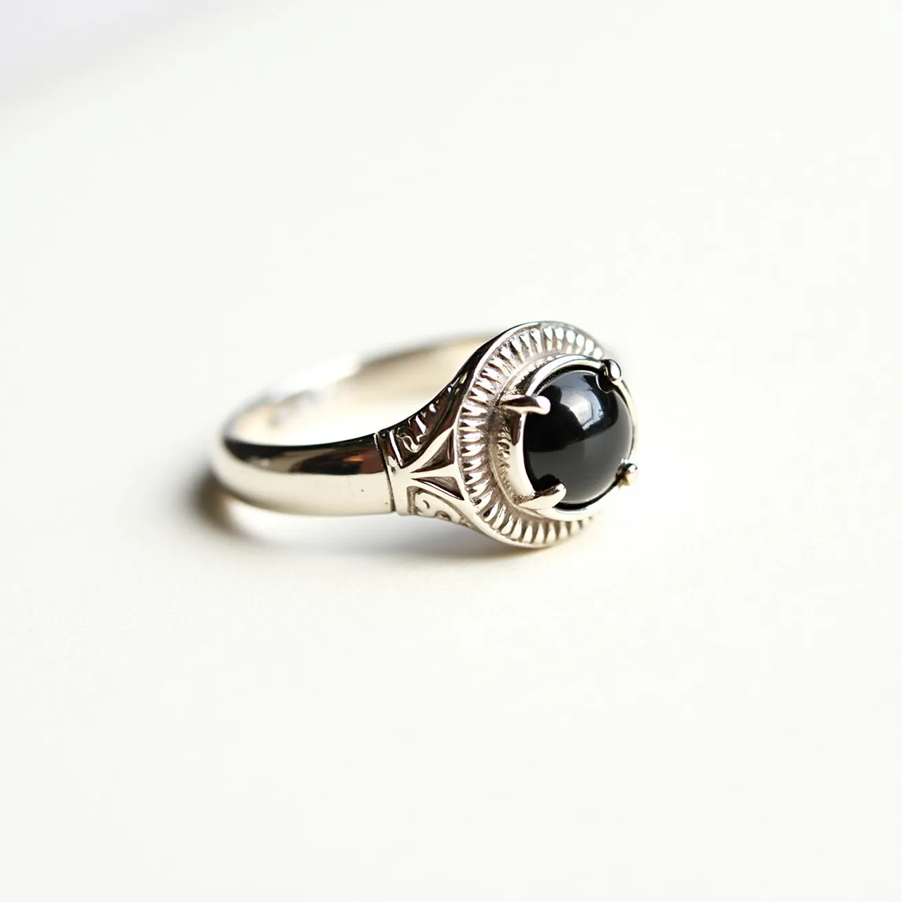 This men's pinky ring features a polished silver band adorned with intricate engravings. At its center, a glossy black cabochon stone is set in a bezel, held securely by four prongs. The cabochon's smooth, dome-like surface adds a touch of elegance, while the detailed setting enhances its visual appeal without any visible clasps or other attachments.