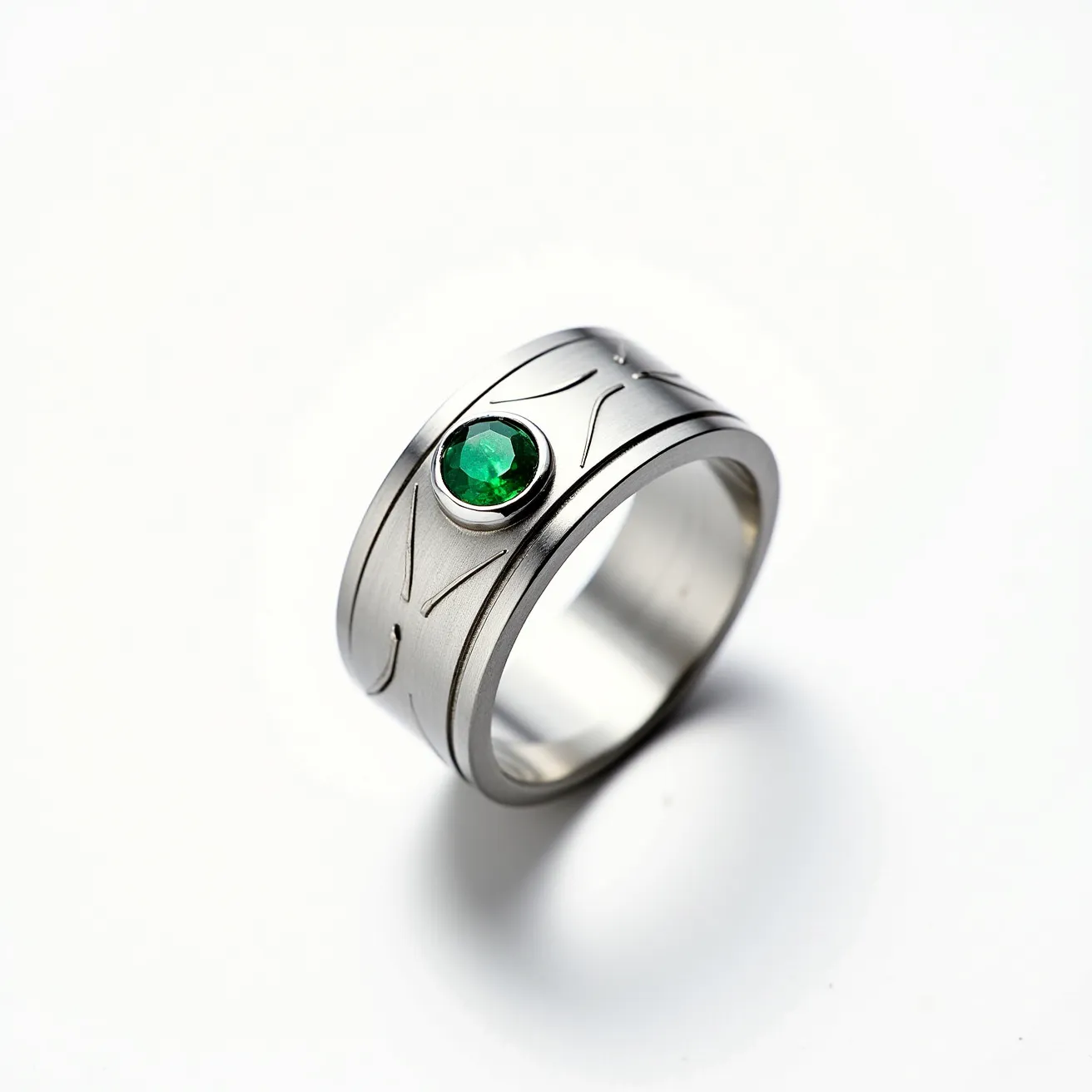 This men's pinky ring features a sleek silver metal band embellished with elegant engraved patterns. It showcases a vibrant green gem, possibly an emerald, which is round-cut and held securely in a bezel setting. The gem adds a striking contrast against the smooth metallic surface, enhancing the ring's sophisticated appearance. There's no visible clasp or additional attachments, emphasizing the ring's simple, elegant design.