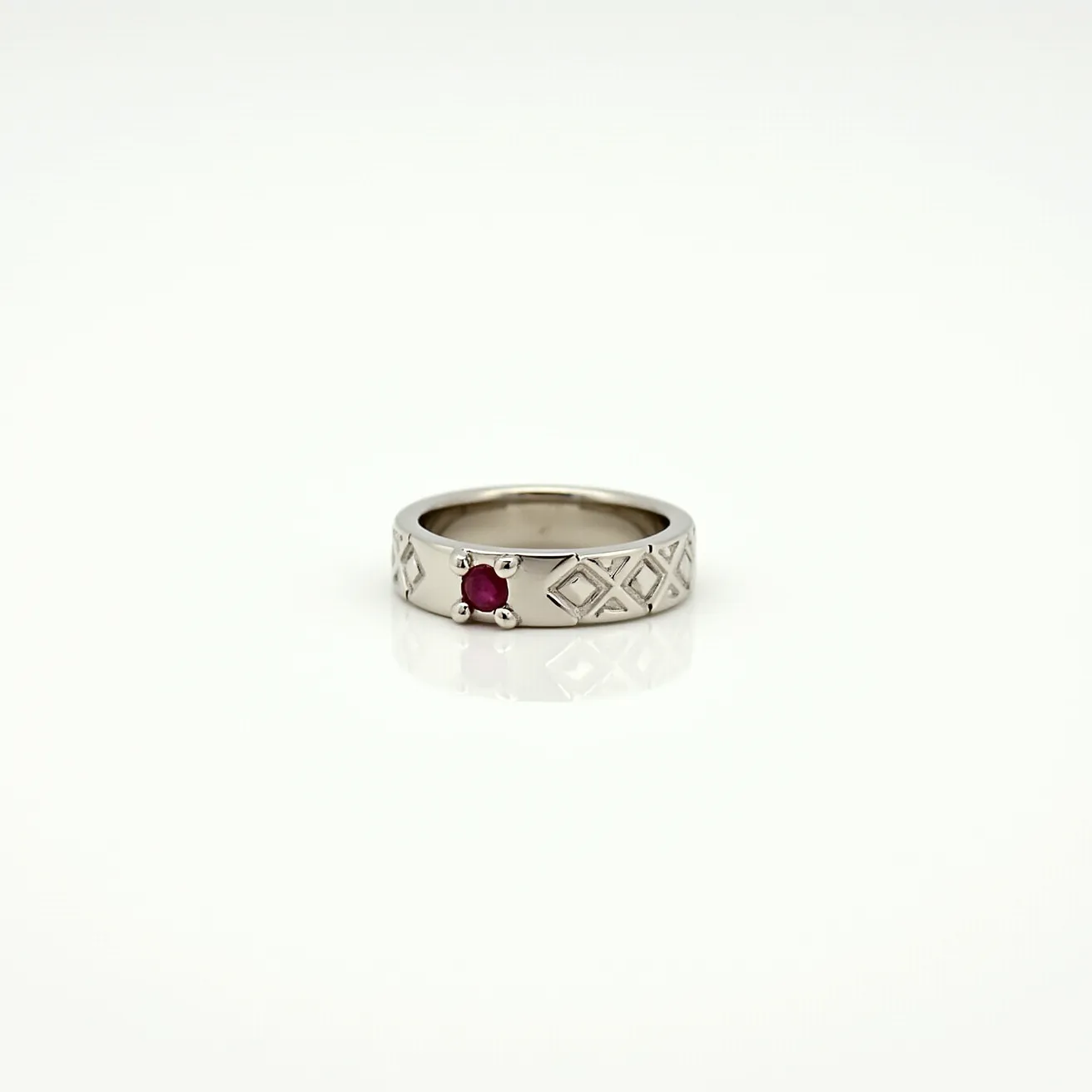 This men's pinky ring features a polished metal band, possibly made of white gold or platinum, which is intricately designed with a repeating geometric pattern. At the center, the ring is set with a small round red gemstone, likely a ruby, held securely in place by a four-prong setting. The band is smooth on the inside, ensuring a comfortable fit. The design and choice of materials suggest a blend of modern aesthetics with classic touches, making it a striking accessory.