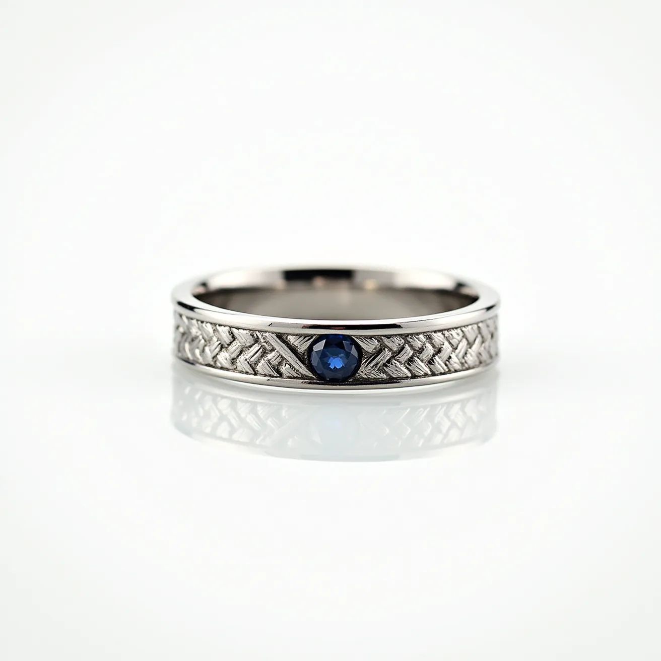 This men's ring features a sleek band made of polished metal, possibly white gold or platinum, which provides a refined and elegant appearance. At the center, it showcases a round blue sapphire, expertly set in a bezel setting that offers both security and a contemporary aesthetic. The band is embossed with a subtle woven pattern, adding texture and a touch of sophistication to the overall design. There are no visible clasps or attachments, emphasizing its simplicity and ensuring it slips on smoothly.