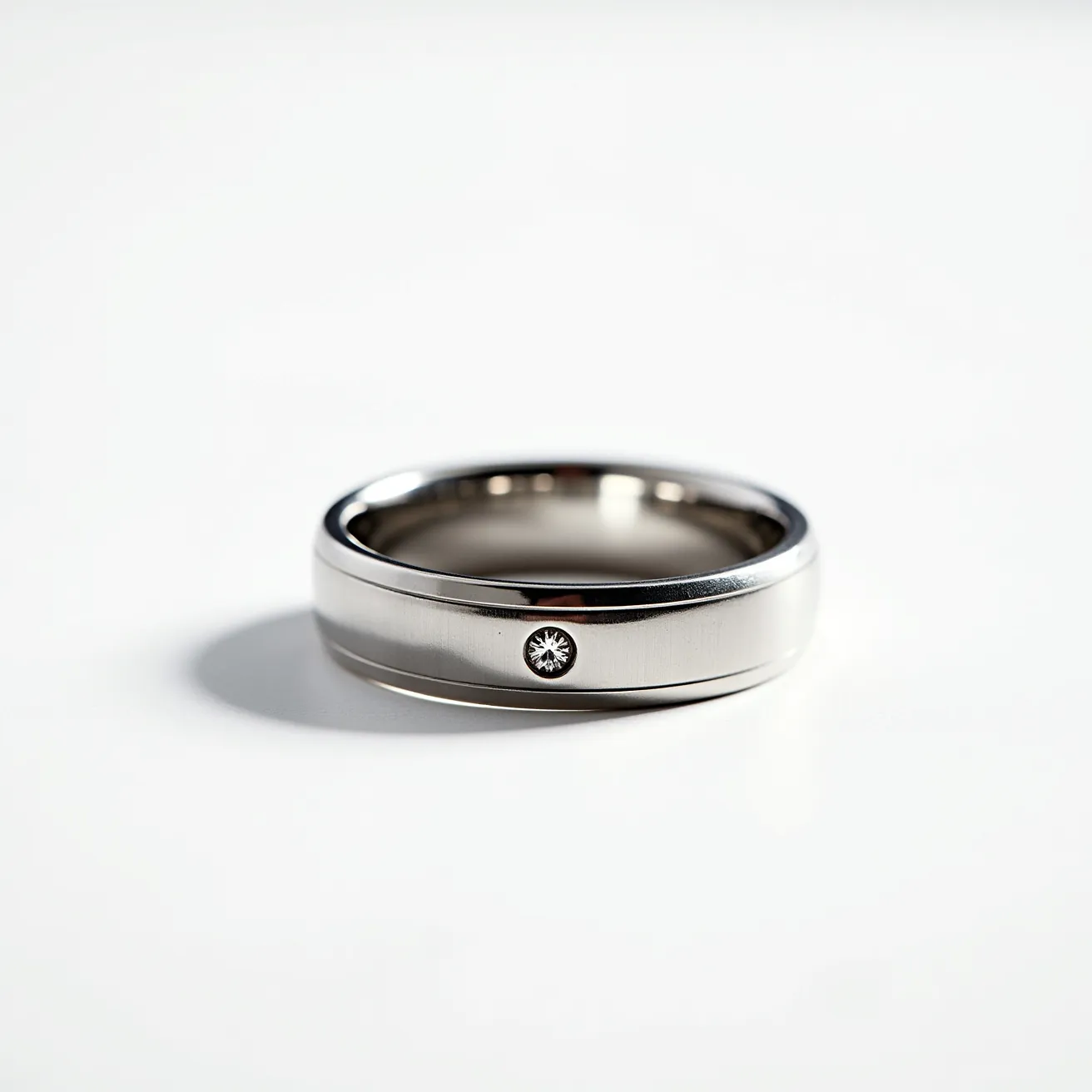 This men's ring is crafted from a polished, silver-toned metal, likely platinum or white gold, giving it a sleek and modern appearance. It features a single, small round-cut diamond set into the band with a bezel setting, adding a subtle touch of elegance and luxury. The ring's design is simple and understated, emphasizing the beauty of the material and the solitary diamond. The interior of the band is smooth, offering comfort for the wearer, and there are no additional clasps or attachments, highlighting its continuous, unbroken form.