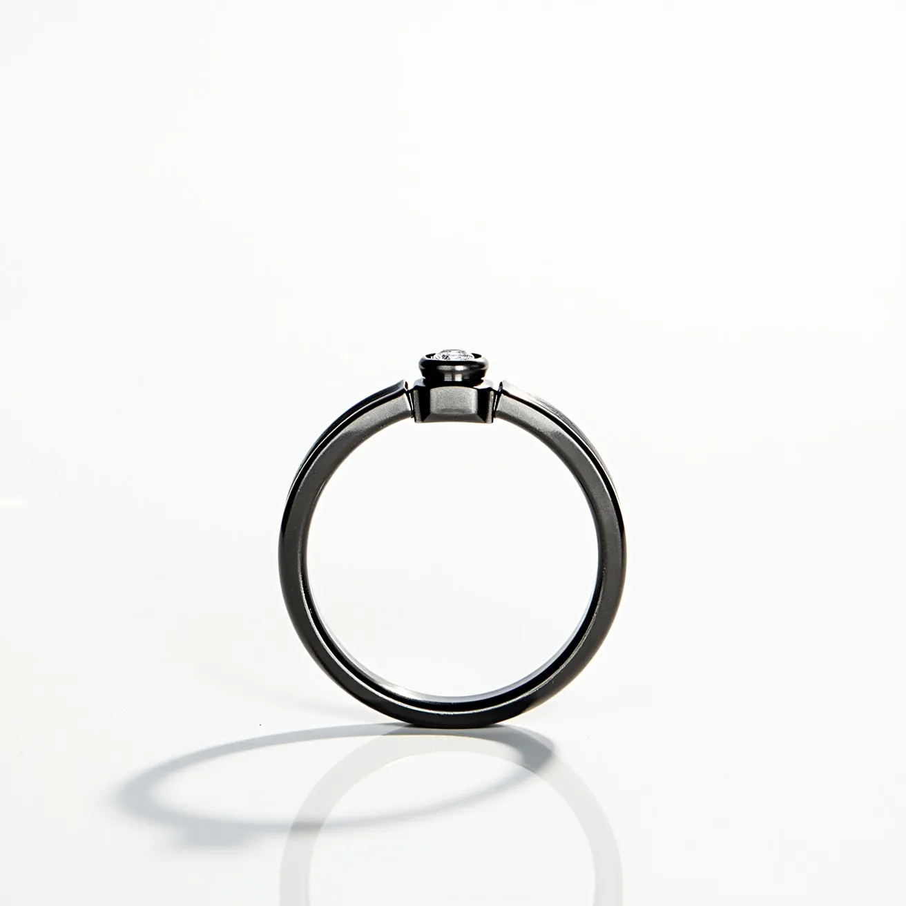 This men's ring features a sleek and sophisticated design in a dark metal, possibly tungsten or titanium, known for their durability and contemporary appeal. At the center, a single round cut gem, likely a diamond or a clear gemstone, is securely set in a bezel setting which provides both protection and a modern aesthetic. The band is smooth and polished, offering a minimalist yet bold look that is both timeless and versatile. The absence of visible clasps or attachments suggests a seamless, continuous circular structure that enhances its refined elegance.