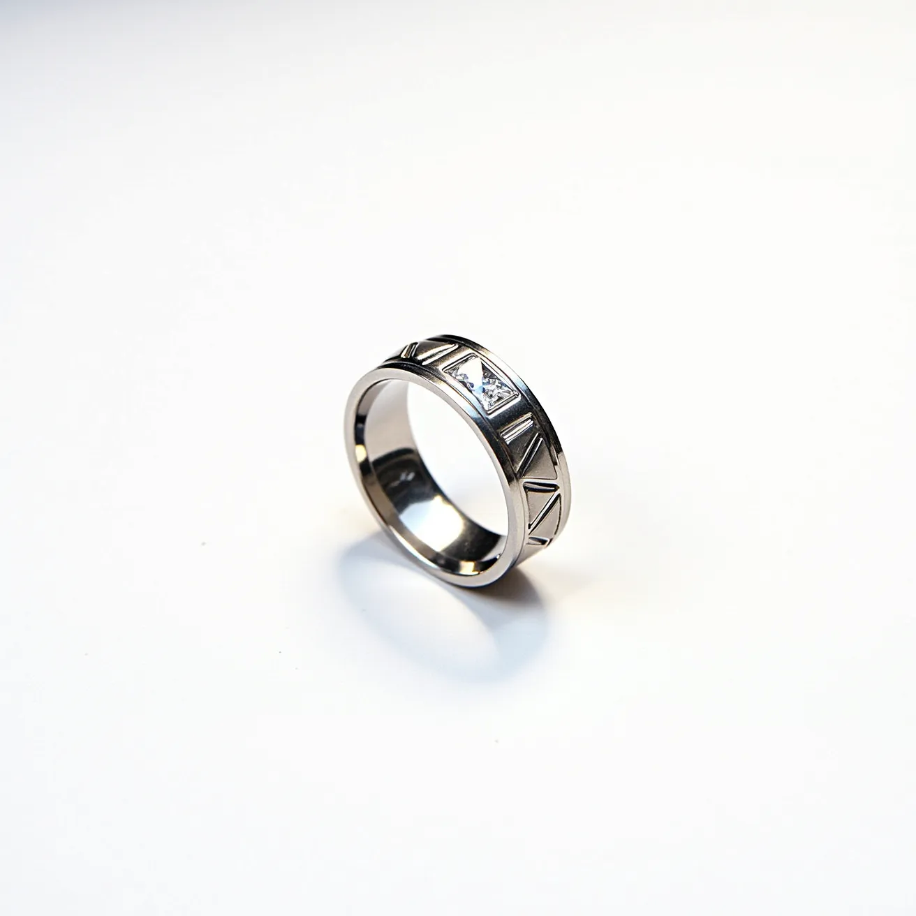 This men's ring features a sleek silver band, likely crafted from stainless steel or sterling silver, providing a modern and durable appearance. The band is adorned with a single, small square-cut gemstone, possibly a diamond or cubic zirconia, set into the surface in a flush setting to create a seamless look. The design includes a series of engraved triangular patterns around the circumference, adding a geometric and stylish touch to the piece. The lack of clasps or additional attachments keeps the focus on the clean lines and minimalist elegance of the ring.