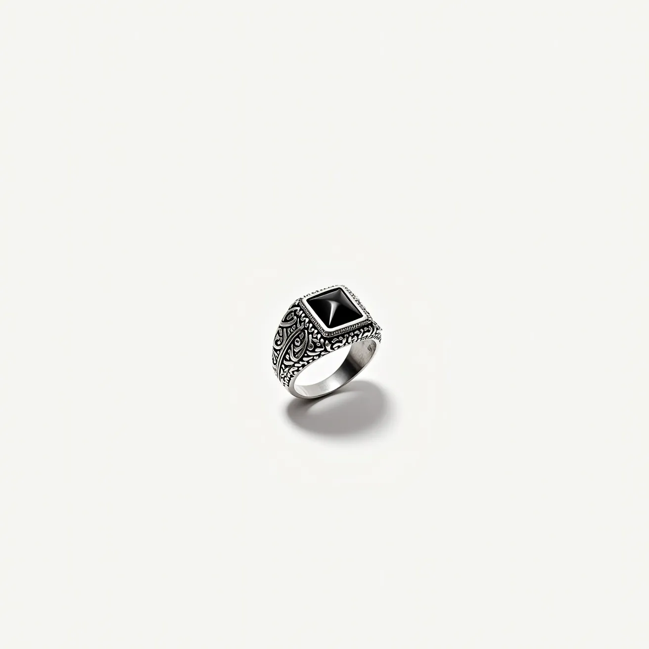 This men's silver ring features an intricately detailed band with ornate engravings that highlight its craftsmanship. The centerpiece is a striking black gemstone, possibly onyx or a similar stone, cut into a pyramid shape and set into a bezel setting that securely holds the stone while showcasing its angular design. The combination of the polished silver and dark gem creates a bold contrast, enhancing the ring's visual appeal. The ring does not include additional clasps or attachments, emphasizing its classic and streamlined design.