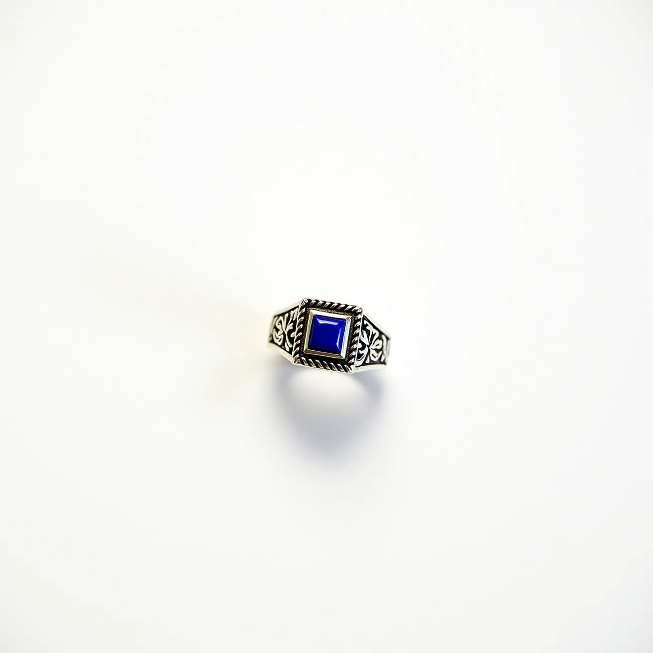 This men's silver ring features an intricate design, showcasing a prominent square-cut blue stone at its center, set into a detailed bezel setting that enhances its elegance. The band displays ornate patterns, possibly etched or engraved, adding to its decorative charm. The silver material provides a sleek and polished appearance, highlighting the vibrant hue of the blue stone.