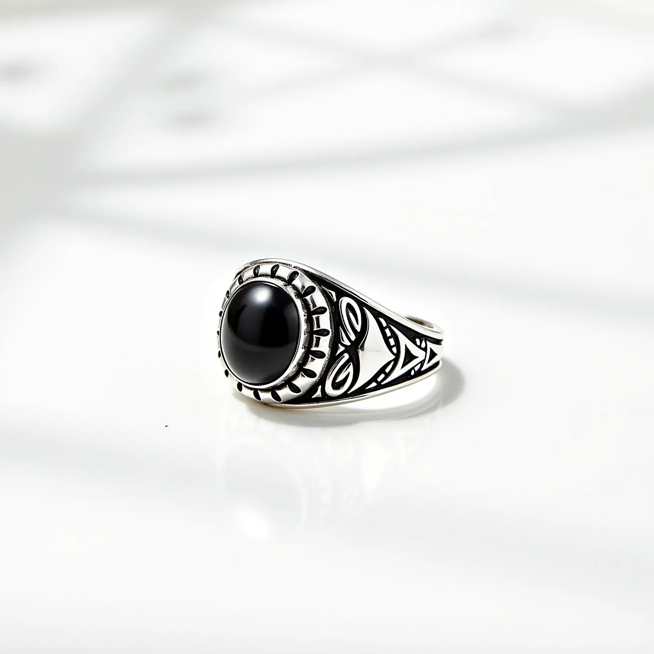 This men's silver ring features an elegant design with a prominent black onyx gemstone set at its center. The stone is round and smoothly polished, exhibiting a cabochon cut that enhances its glossy sheen. The gemstone is securely held in place by a decorative bezel setting, which also features detailed etchings complementing the ring's overall aesthetic. The band's shoulders are adorned with intricate patterns, adding an artistic flair to the piece. Crafted primarily from high-quality silver, this ring combines the understated elegance of the metal with the bold presence of the onyx, making it a standout accessory.