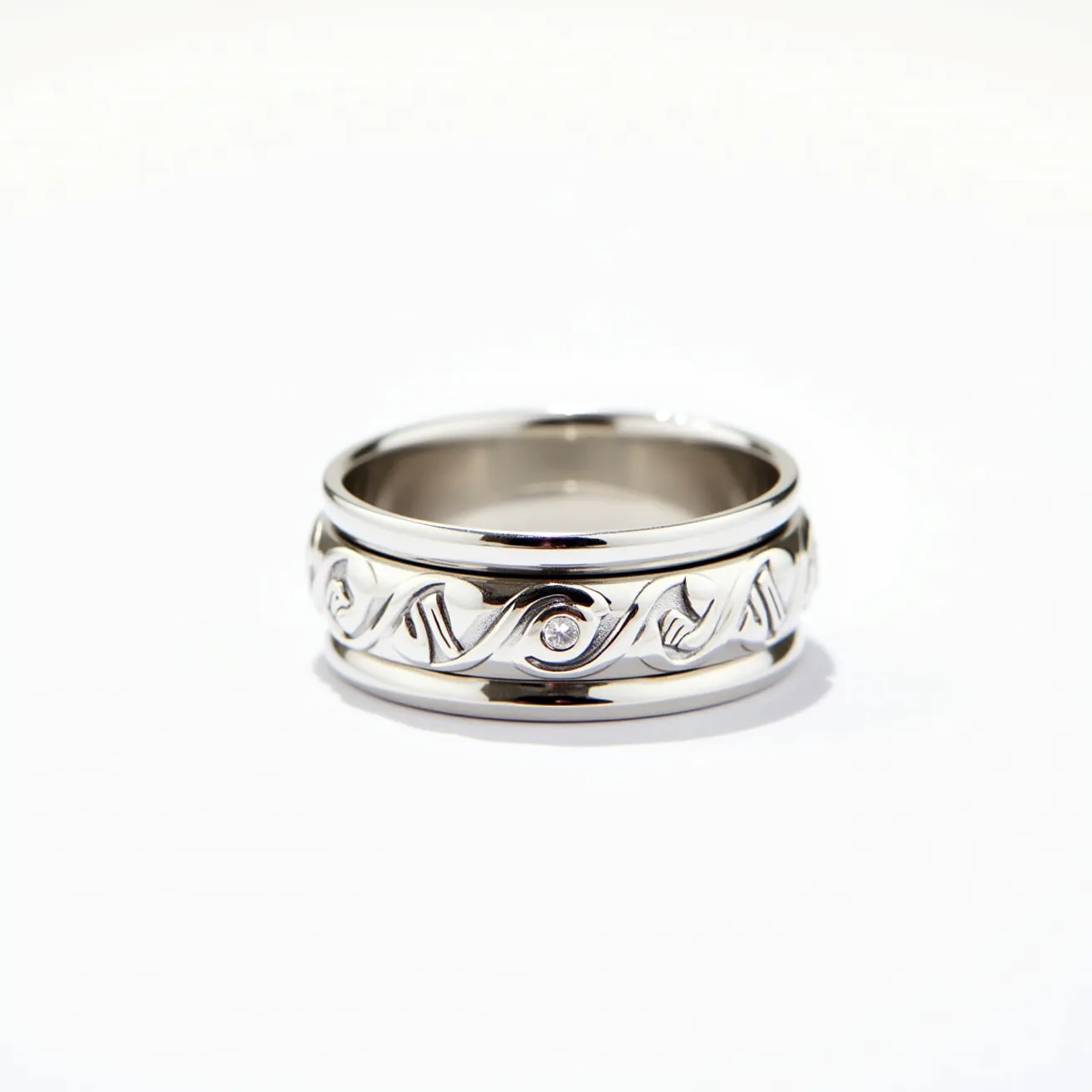 This men's spinner ring is crafted from a polished silver-toned metal, featuring a central band with intricate, swirling patterns. The design is accentuated by a small, round-cut gemstone, securely set in a bezel setting, offering a subtle sparkle. The outer band freely rotates around the inner band, showcasing the spinner design feature. The ring has a smooth and polished finish, reflecting its quality craftsmanship and sleek aesthetic.