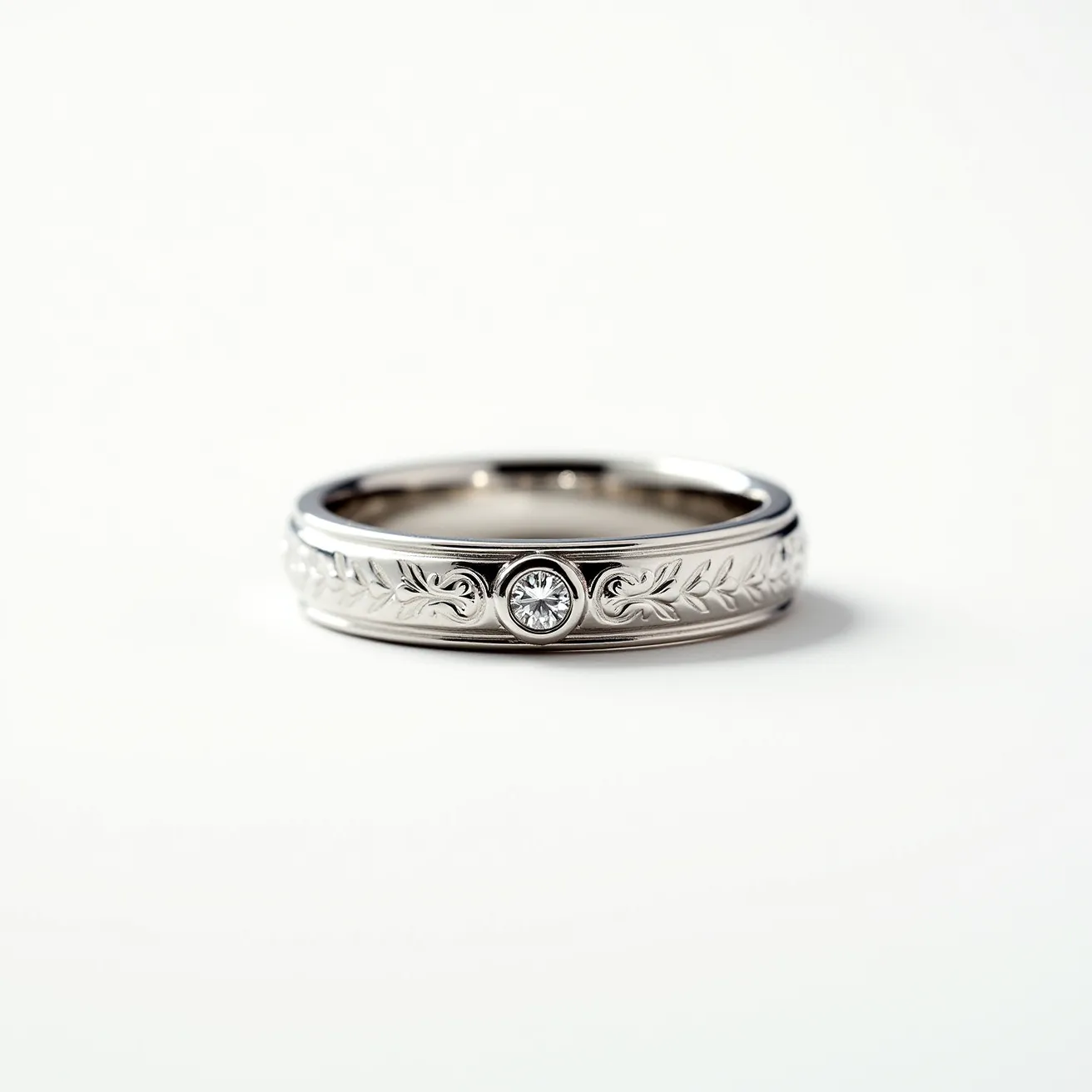 This men's wedding band is crafted from what appears to be white gold or platinum, showcasing a polished finish that enhances its elegance. The band features an intricate engraved pattern of leaves, adding a touch of sophistication and uniqueness. At the center, a small round-cut diamond is securely set in a bezel setting, providing a subtle yet eye-catching sparkle. The design is seamless, smooth, and without any visible clasps or attachments, emphasizing a continuous loop that symbolizes eternity.