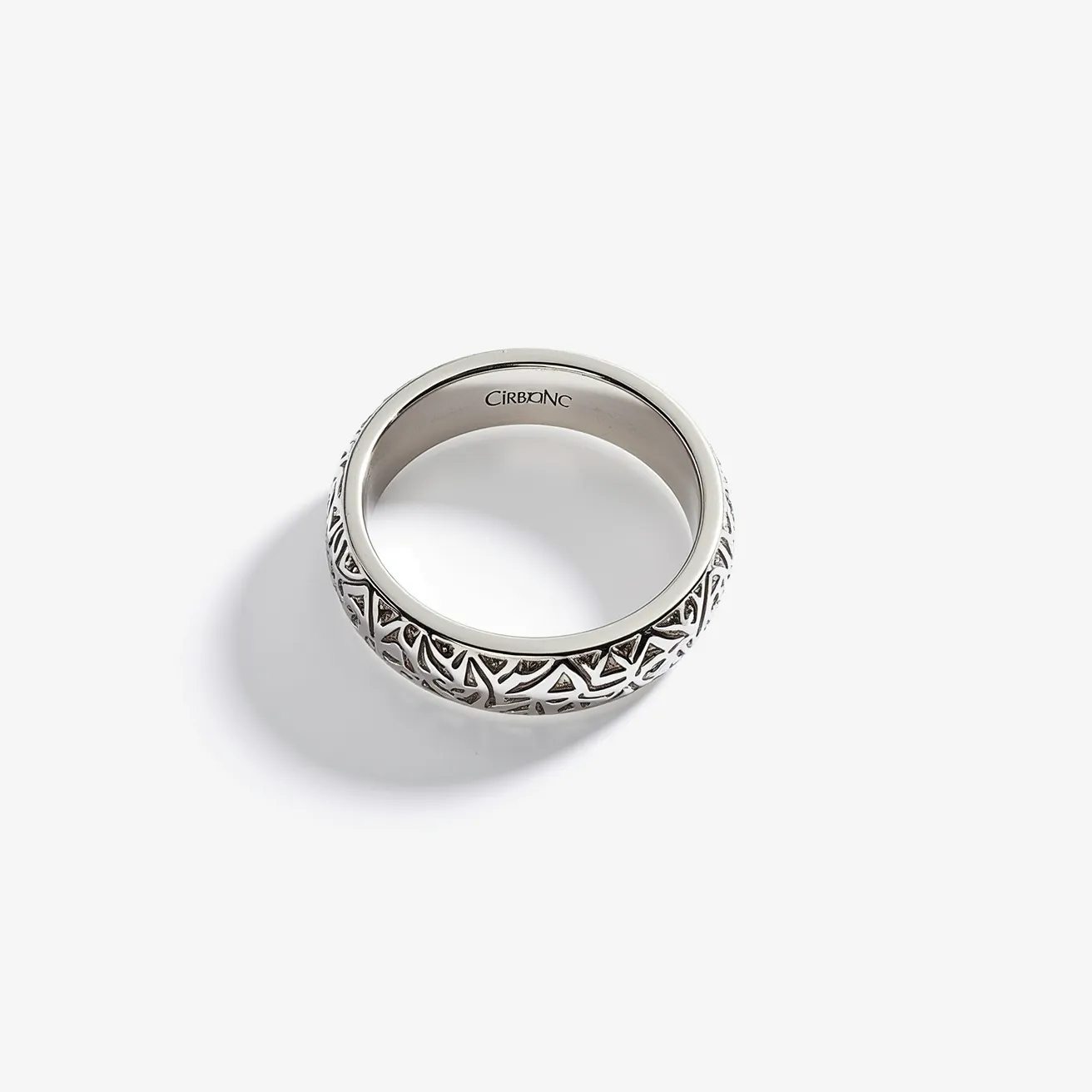 This men's wedding band is crafted from a silver-toned metal, exuding a sleek and modern aesthetic. It features an intricate pattern of triangular motifs etched around its circumference, adding a touch of detailed artistry. The interior of the band is smooth and engraved with the word "Cirbonac," suggesting a brand or designer's name. There are no visible gems or stones incorporated into the design, and the band appears as a continuous loop without any clasps or attachments, embodying a classic and seamless ring structure.