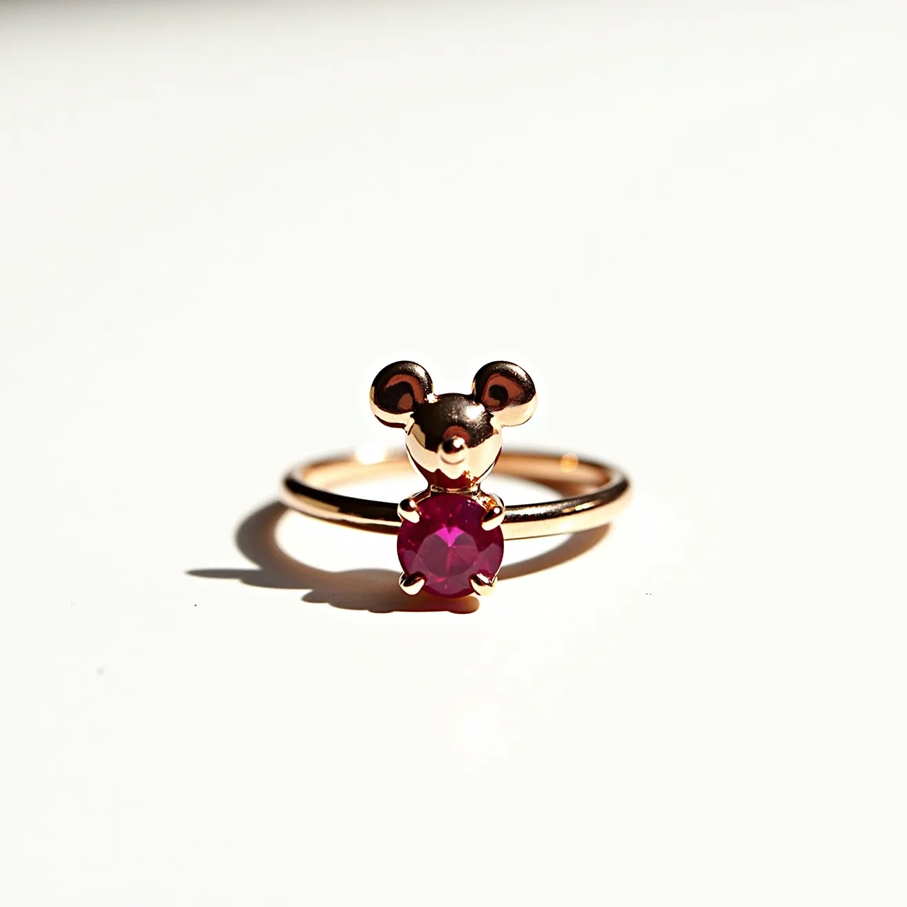 This Mickey Mouse ring features a charming design with the iconic silhouette of Mickey's head and ears crafted from what appears to be a polished gold. The ring showcases a vibrant round-cut pink gemstone set at the base of Mickey's head, likely held securely in place by four prongs. This gem adds a pop of color and enhances the playful character of the piece. The band is simple and elegant, without any additional adornments or clasps, allowing the central design to stand out prominently. The overall craftsmanship suggests a blend of playful nostalgia with fine jewelry aesthetics.