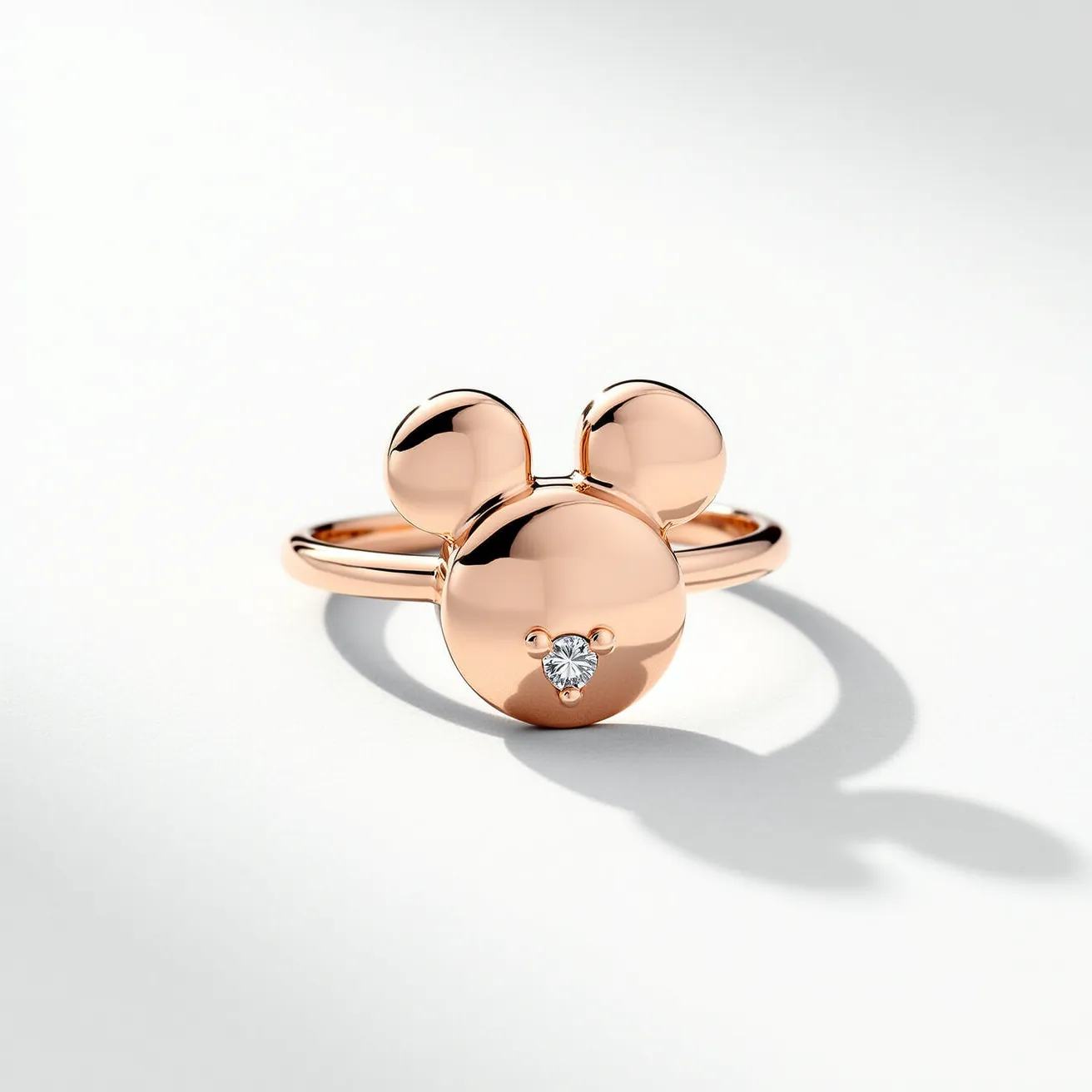 This Mickey Mouse ring features a sleek design crafted from polished rose gold, forming the iconic silhouette of Mickey's head, complete with prominent circular ears. At the center of the head, a small, round-cut diamond is set, adding a touch of sparkle and elegance to the piece. The diamond is held securely in place by a simple prong setting, ensuring it remains the focal point of the ring. The band is smooth and unadorned, allowing the Mickey Mouse emblem to stand out as the primary feature of the ring.