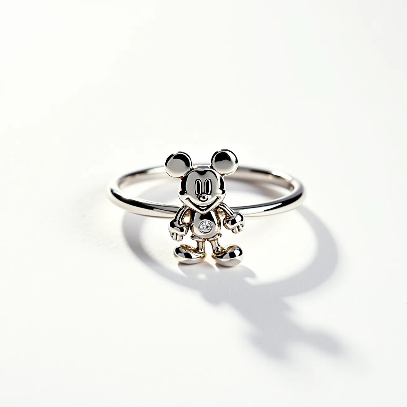 This Mickey Mouse ring features a finely crafted character design in shiny metal, likely silver or white gold, adding a sleek and polished look. The ring’s focal point is a small, round-cut gem set in the center of Mickey Mouse's torso, which is bezel-set for a secure and refined appearance. The band is simple and unadorned, complementing the character without distraction. The ring lacks any additional clasps or attachments, allowing for a continuous and smooth design ideal for seamless wear.