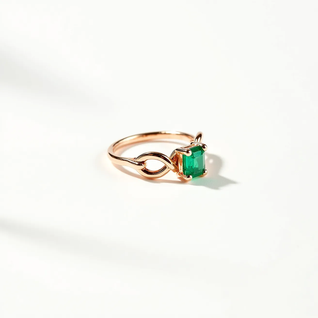 This midi ring features a delicate and minimalist design crafted from rose gold metal. It showcases an emerald-cut green gemstone, securely held in place by a four-prong setting. The band subtly incorporates an artistic design element that adds an elegant twist to its style. The combination of the warm rose gold and the vivid green stone creates a striking visual contrast, enhancing the ring's sophistication.