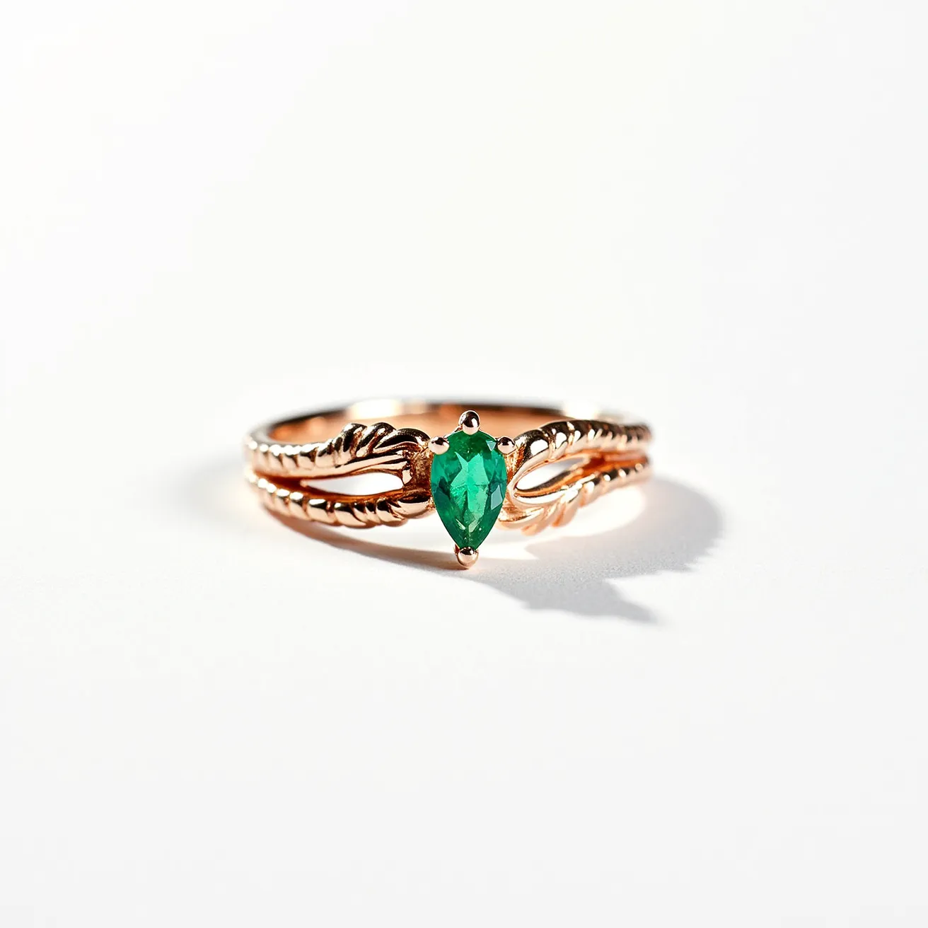 This midi ring features a delicate design crafted from rose gold, with intricate detailing along the band's surface. It is adorned with a pear-shaped green gemstone, possibly an emerald, securely set in a prong setting that highlights the stone's vibrancy and elegance. The band is artistically crafted with twisted and ornate patterns, giving it a unique and refined appearance. There is no clasp or additional attachment, maintaining a seamless and continuous loop in its design.