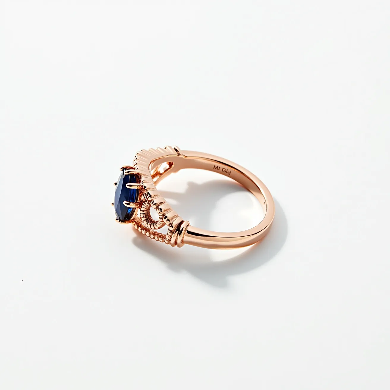 This midi ring features a band made from a rose gold material, exhibiting a warm, lustrous finish. The centerpiece is an oval-cut dark blue gemstone, securely held in place by a series of prongs, suggesting a traditional claw setting. The band is adorned with intricate details, including a scalloped design that enhances the overall elegance of the ring. Markings inside the band indicate the metal's composition, adding an element of authenticity and quality.