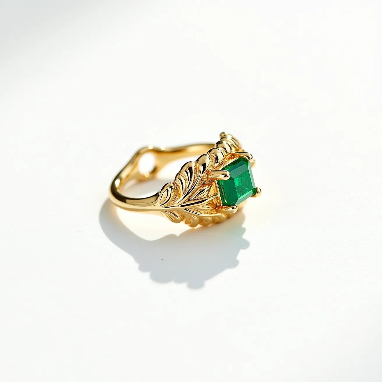 This midi ring features a gold band with intricate, decorative leaf patterns, enhancing its elegant design. At its center, it showcases an emerald green stone with an emerald cut, securely set in a classic prong setting. The prongs, made of the same gold material, hold the gem prominently, allowing light to pass through the stone and highlight its rich, vibrant color. The ring has a graceful, adjustable structure accommodating a variety of finger sizes without a specific clasp or closure mechanism. The combination of the gold and the green stone creates a striking contrast, contributing to the ring's overall sophisticated and luxurious aesthetic.