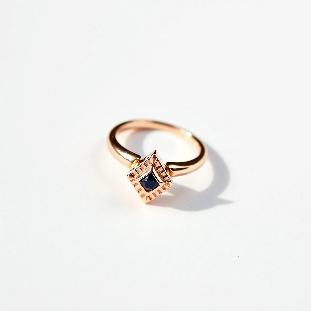 This midi ring features a band crafted from polished gold, exuding a sleek and sophisticated appearance. At its center sits a striking black gemstone, which appears to be square-cut and elegantly set in a bezel setting, enhancing its reflective qualities and protecting the stone's edges. The setting itself is surrounded by an intricately detailed gold bezel that adds an artistic and textured dimension to the piece. There are no clasps or additional attachments, allowing the design to maintain its simplicity and elegance.