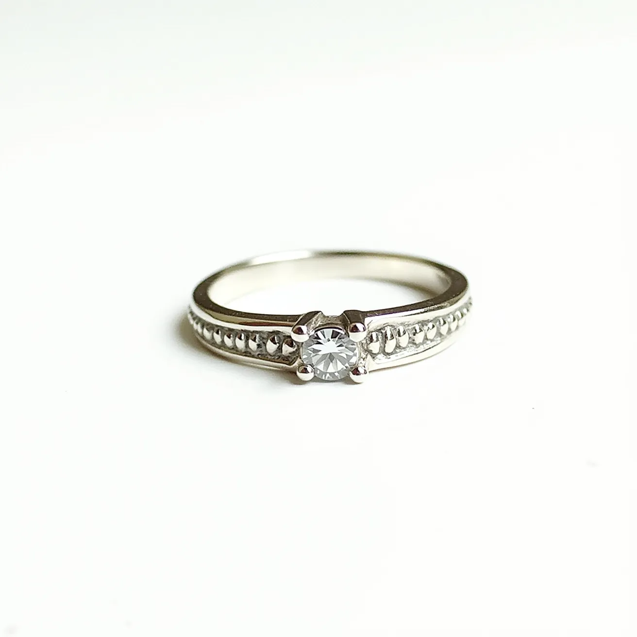 This moissanite promise ring features a central round moissanite gemstone, elegantly held in place by a classic four-prong setting. The band appears to be made of a lustrous metal, likely sterling silver or white gold, which enhances the brilliance of the central stone. The shank of the ring is adorned with delicate milgrain detailing and a row of smaller decorative elements, adding a touch of vintage-inspired elegance to the design. The overall craftsmanship suggests a seamless blend of traditional and contemporary styles, making it a timeless symbol of commitment.