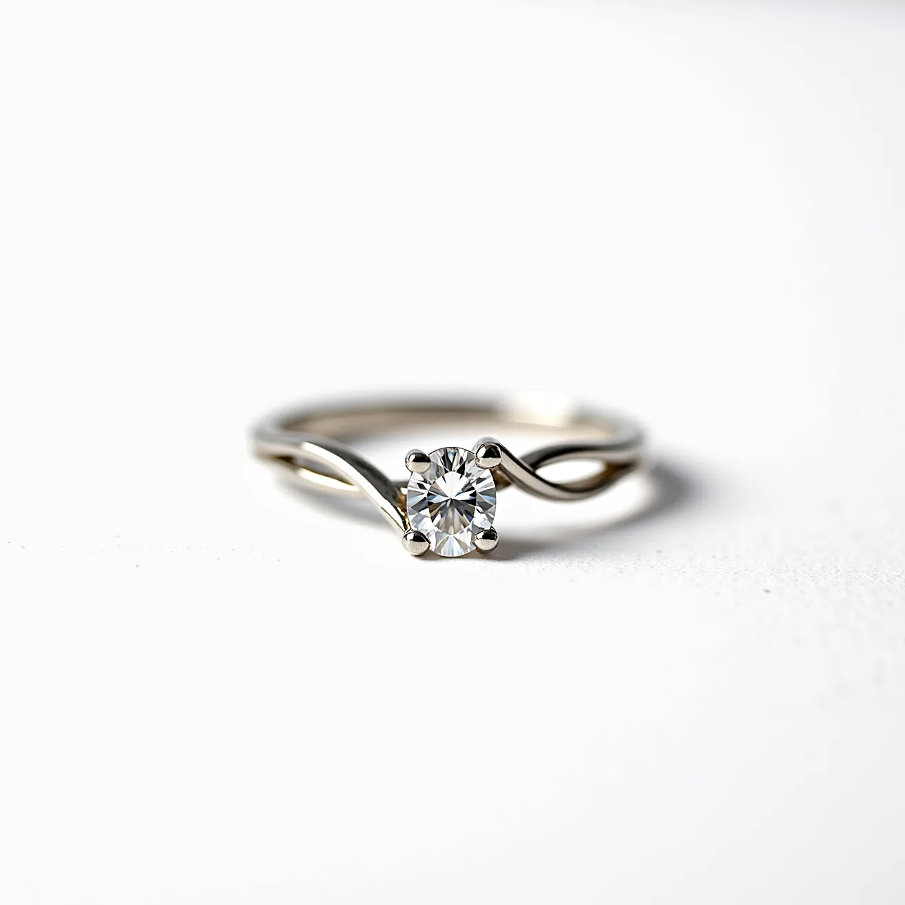 This moissanite ring features a central round-cut moissanite stone, which is elegantly set in a classic four-prong setting, allowing the gem to capture and reflect light brilliantly. The band is crafted from metal, possibly platinum or white gold, exhibiting a smooth and polished finish. The band design incorporates a twisted or split-shank style, adding an intricate visual element and enhancing the ring's aesthetic appeal.