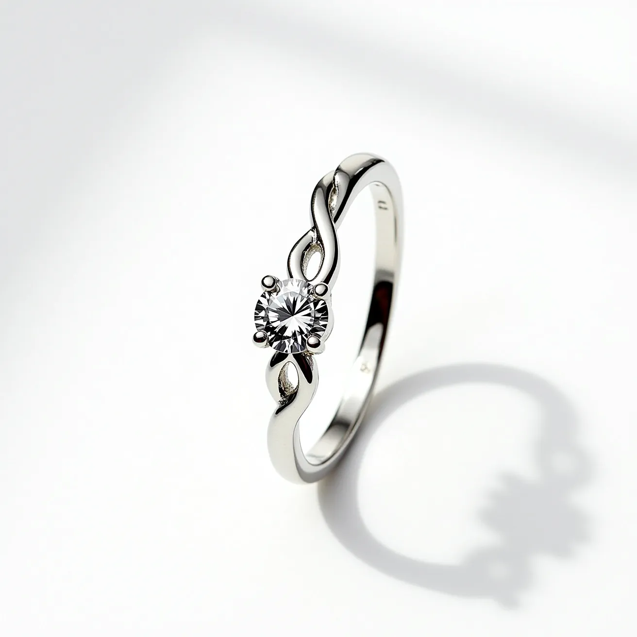 This moissanite ring features a sleek, polished metal band, likely made of white gold or platinum, which elegantly twists into an infinity design. The focal point is a round-cut moissanite stone, securely held in place by a four-prong setting. The prong setting allows the stone's brilliance to shine, emphasizing its clarity and sparkle. The twisting band adds a unique touch to the design, combining modern elements with a classic style. The overall craftsmanship suggests durability and elegance, making it a standout piece.