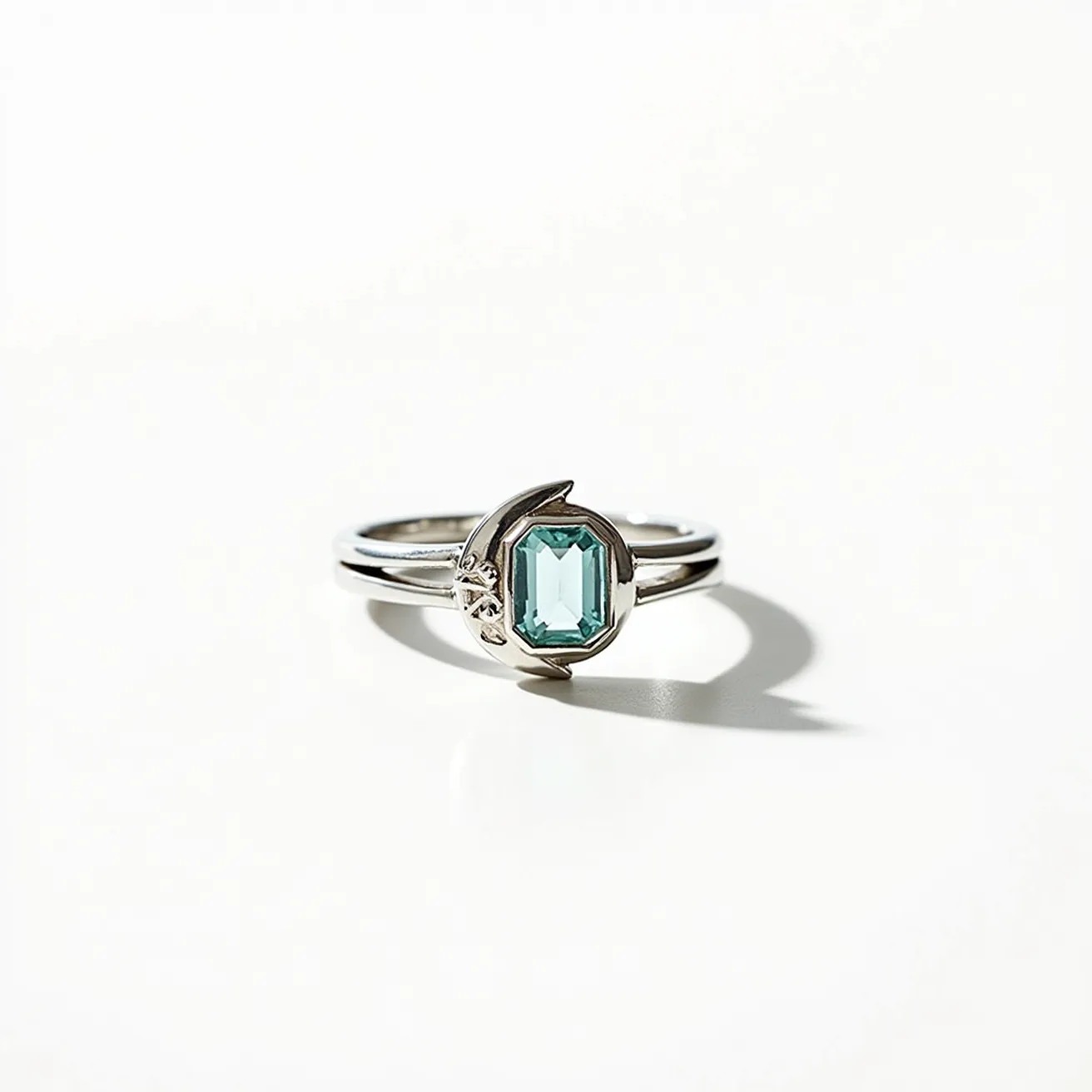 This moon ring features a sleek silver band delicately crafted with a minimalist design. The centerpiece is an exquisite emerald-cut gemstone, likely aquamarine or a similar green-blue stone, set within a gleaming bezel setting that resembles a crescent moon. The prongs secure the gemstone gracefully, highlighting the stone’s clarity and sophisticated cut. This elegant piece captures a celestial theme, combining the cool hues of the gemstone and the lunar-inspired design in the metalwork to create a harmonious, ethereal aesthetic.