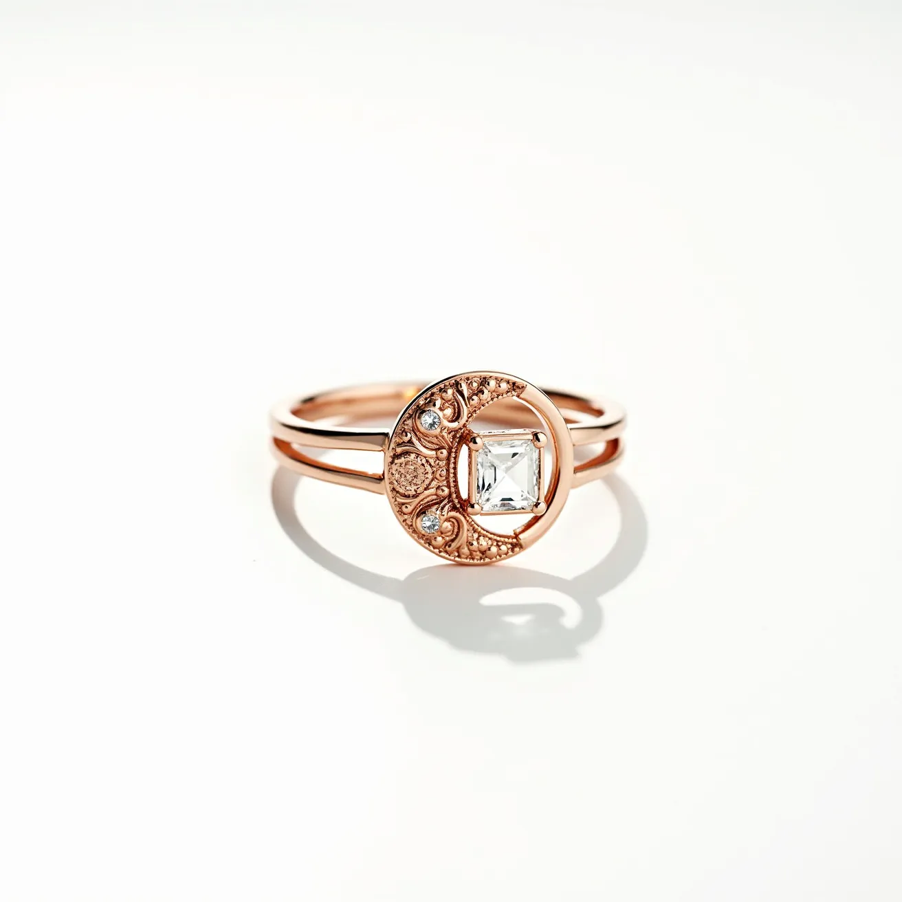 This moon ring features a delicate crescent motif crafted in a warm rose gold tone. The crescent, adorned with intricate textures and patterns, holds small round gems set at its points, adding subtle sparkle. At the center, a square-cut, clear gemstone is held in a bezel setting, which enhances its brilliance and modern aesthetic. The ring's band is split, providing an elegant and airy design that complements the celestial theme of the piece.