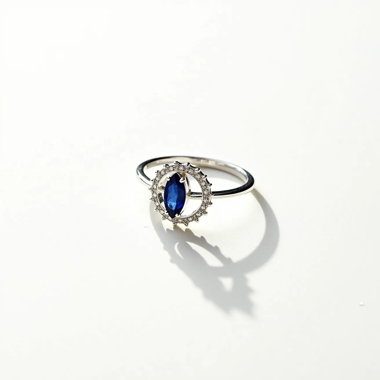 This moon ring features a striking marquise-cut blue sapphire set as its centerpiece, encircled by a delicate halo of small round diamonds or diamond-like stones. The gemstones are prong-set, allowing for maximum light reflection and brilliance. The band is crafted from a polished silver-hued metal, likely white gold or platinum, adding an elegant and timeless appeal. The intricate design and choice of materials suggest a harmonious blend of modern and classic jewelry aesthetics.