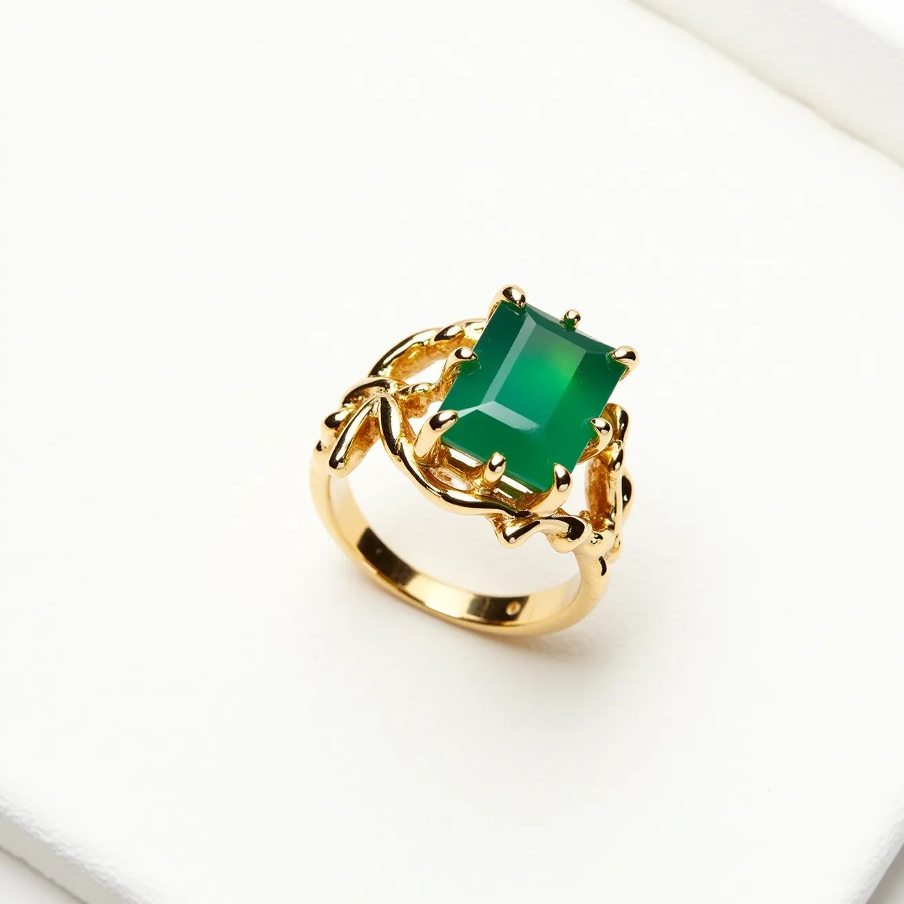 This moss agate ring features a vibrant green rectangular gemstone, likely moss agate, cut in an emerald style that creates an elegant and sophisticated appearance. The stone is securely set in a prong setting that complements the overall design with its intricate golden metalwork, crafted in a leaf-like pattern for added detail and charm. The band appears to be made of gold, which harmonizes beautifully with the green hue of the moss agate, creating a balanced and harmonious look. The prong setting not only secures the gemstone but also enhances its visibility and impact, allowing it to be the focal point of this exquisite piece of jewelry.