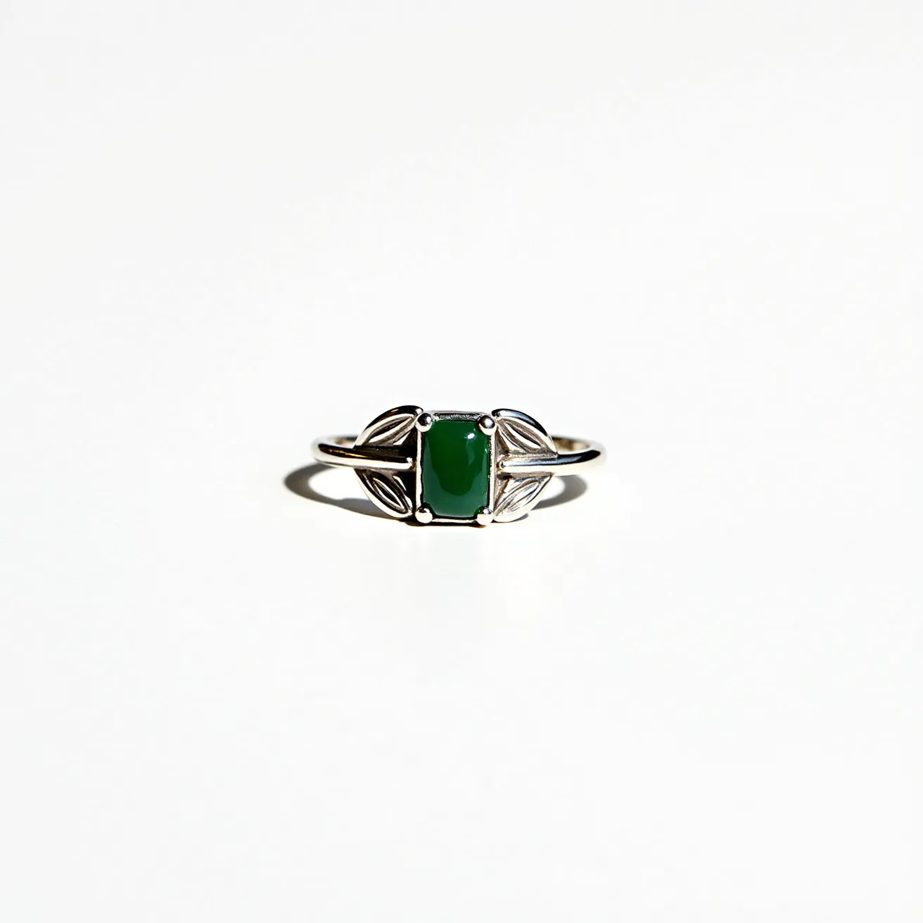 This moss agate ring features a central rectangular stone of polished moss agate, exhibiting its characteristic green and earthy tones. The gem is set in a minimalist bezel setting that highlights its natural beauty. The band appears to be made of sterling silver, with elegant, leaf-like designs on either side of the stone, adding a touch of nature-inspired artistry. The craftsmanship integrates the organic feel of the moss agate with the sleek shine of the silver, creating a harmonious and stylish accessory.