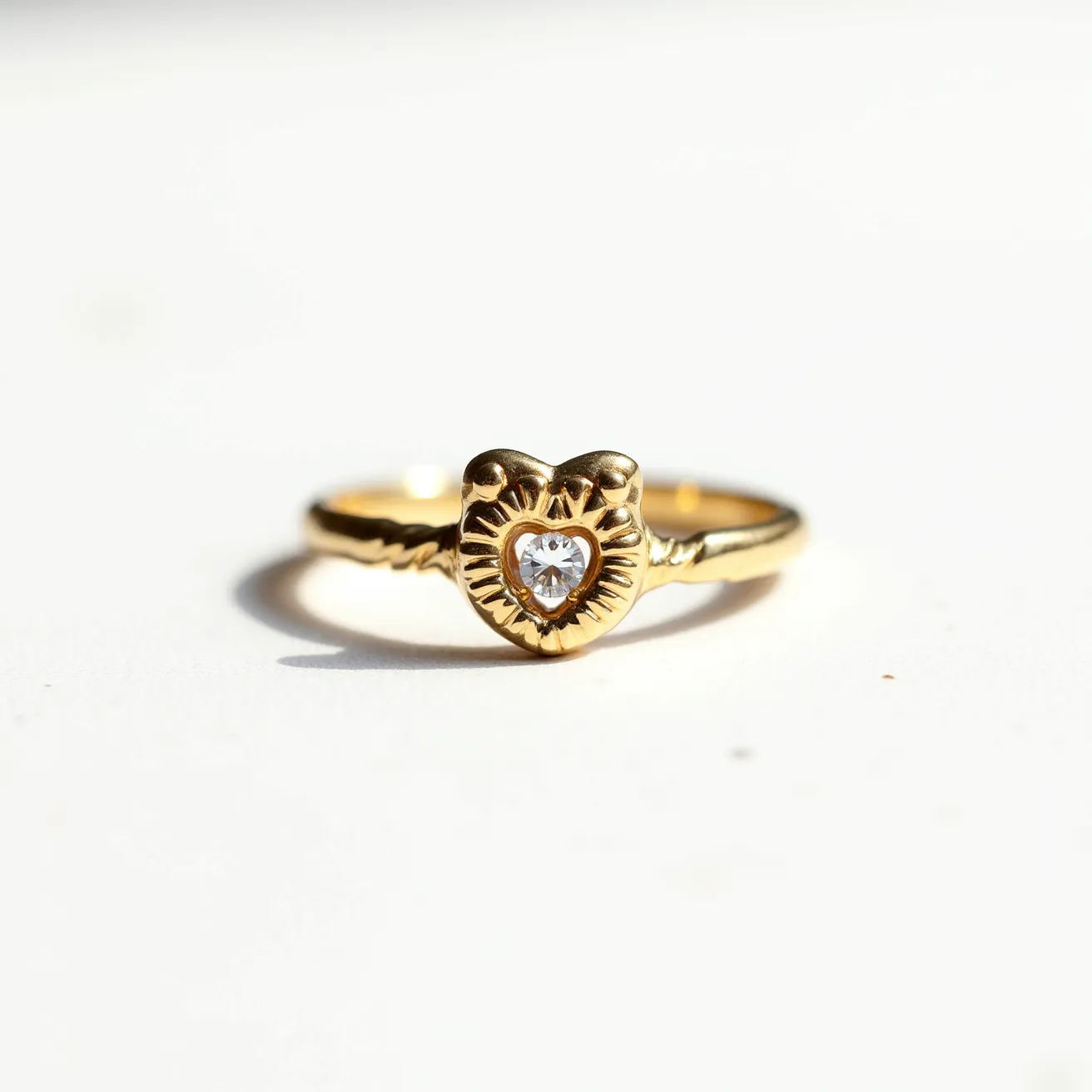 This mothers ring features a gold band with a prominent heart-shaped design at its center. The centerpiece is adorned with a single heart-cut gemstone, securely set within the metal. The ring's design is intricate, with the heart motif surrounded by detailed embellishments that enhance its elegance. The band itself is smooth and glossy, showing off the richness of the gold material.