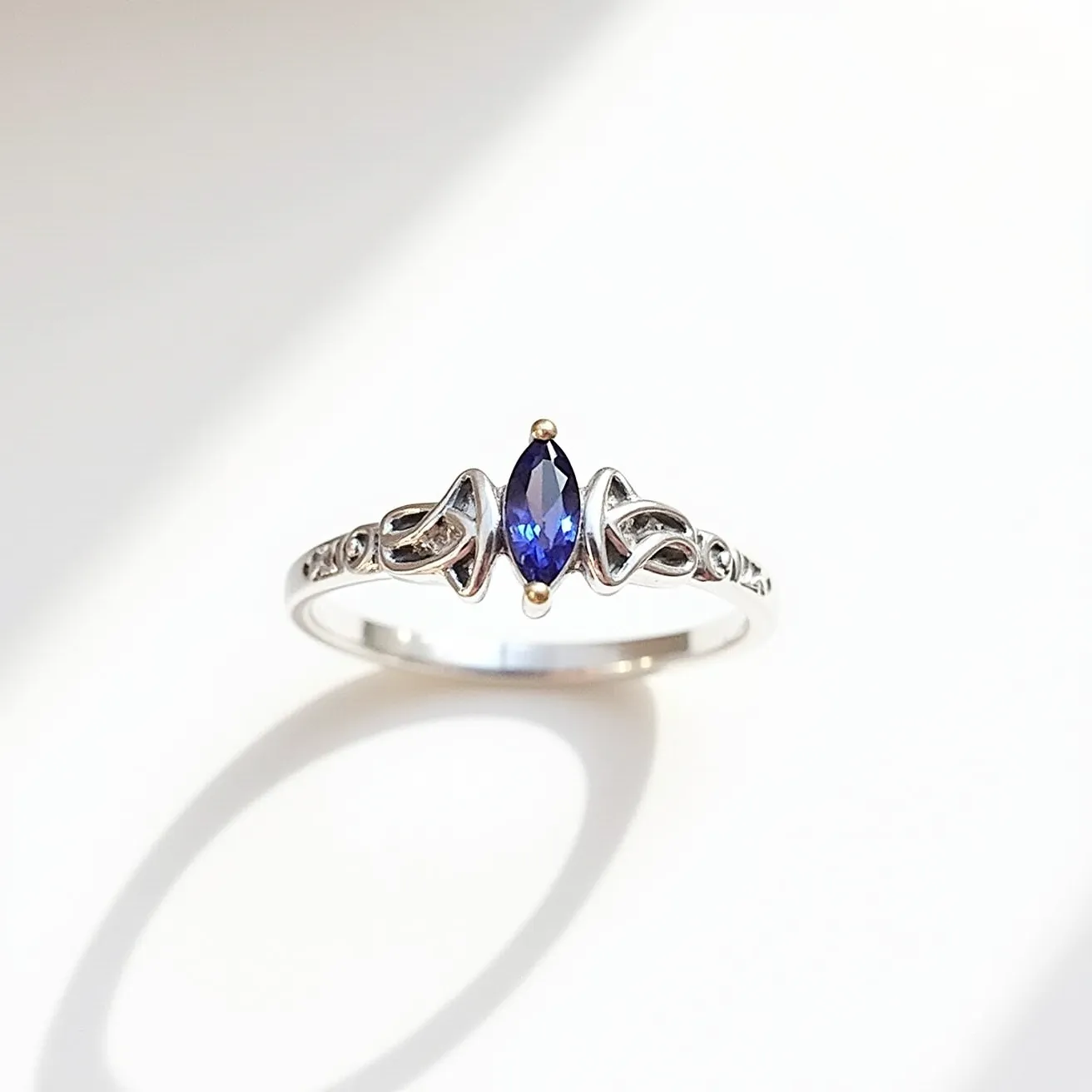 This mothers ring features a sleek silver band with an intricate design that incorporates delicate knotwork motifs. At its center, a marquise-cut blue gemstone is elegantly set in a four-prong setting, adding a striking focal point to the piece. The stone is flanked by the openwork design on both sides of the ring, enhancing its elegance and providing a seamless flow to the overall aesthetic. The ring does not include any additional clasps or attachments, as it is a typical slip-on style ring. The combination of the blue gemstone and the silver band creates a classic yet sophisticated look, suitable for daily wear or special occasions.